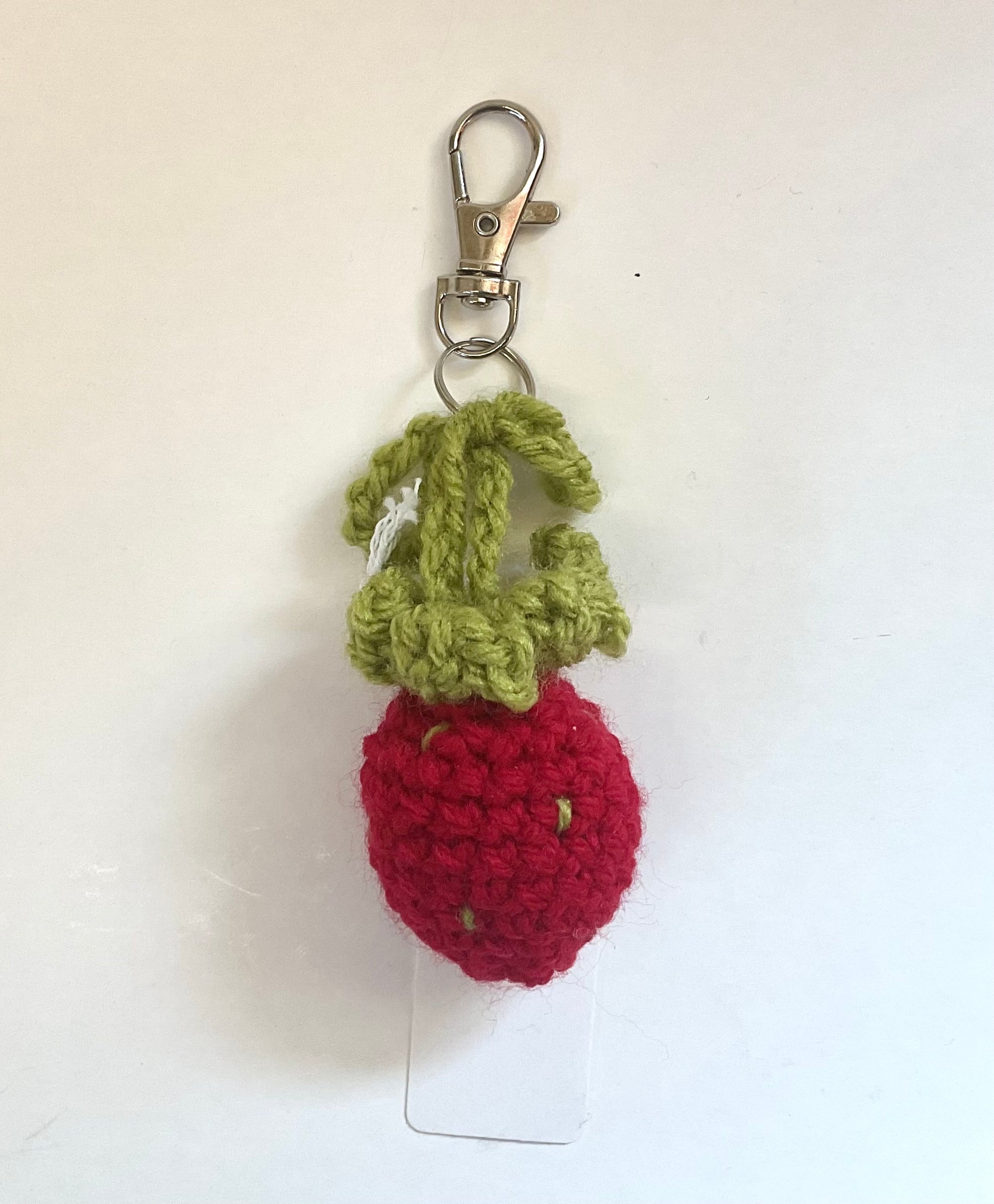Crocheted strawberry keychain with green leaves on a white background