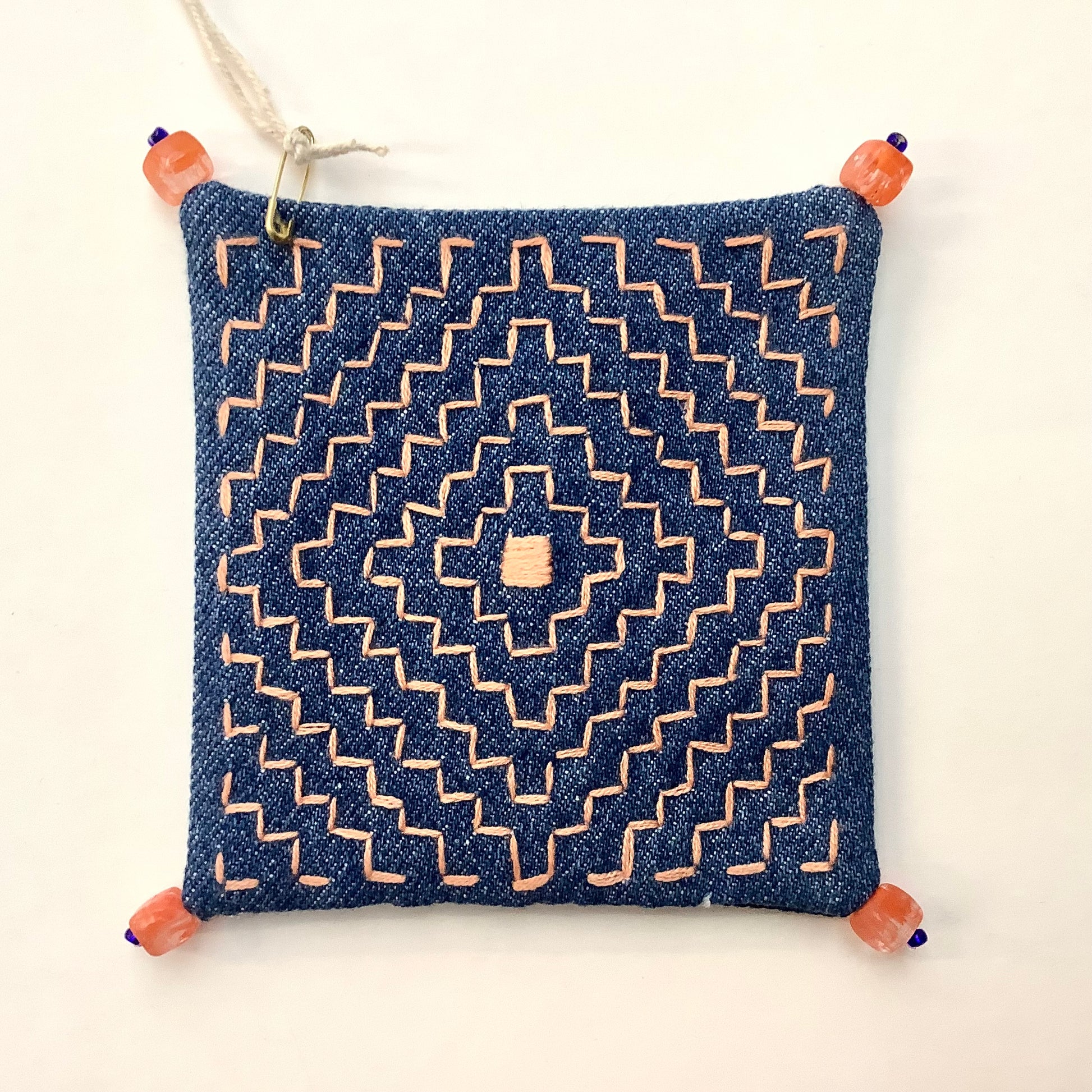 Decoratively stitched denim coaster with a geometric pattern and beads on each corner