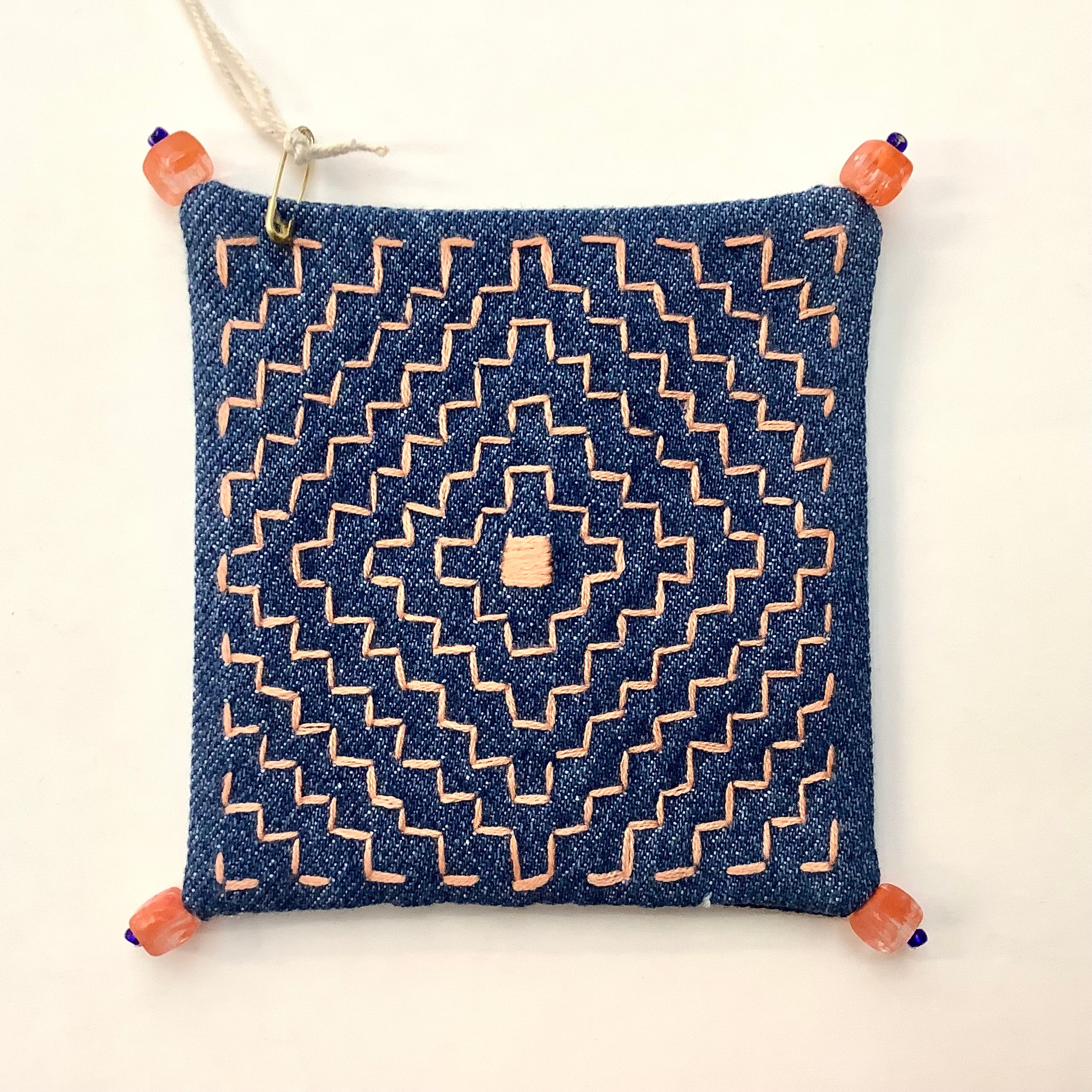 Decoratively stitched denim coaster with a geometric pattern and beads on each corner