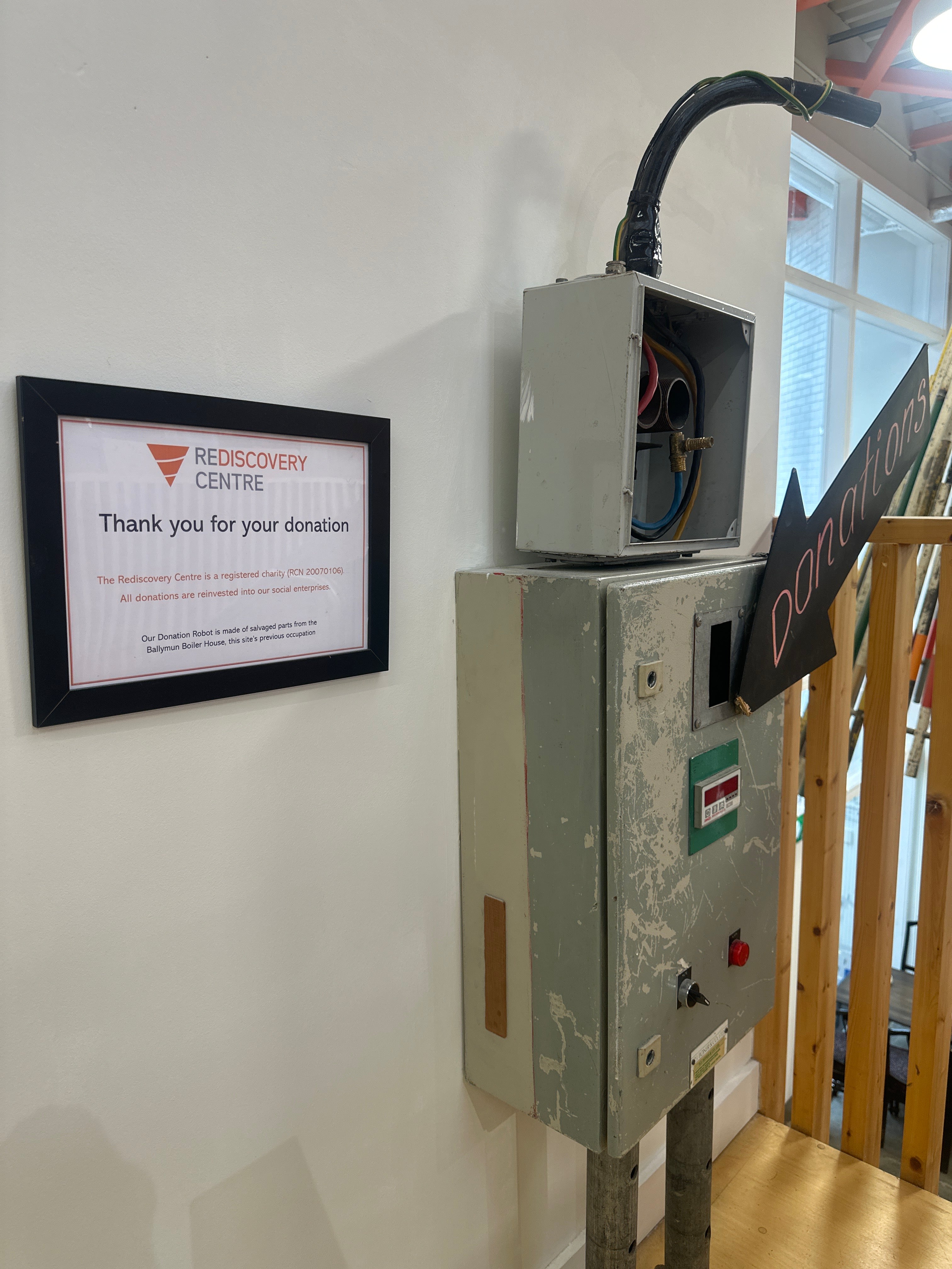 Donation box in the shape of a robot made from a repurposed industrial metal box, with a framed sign thanking visitors for donations