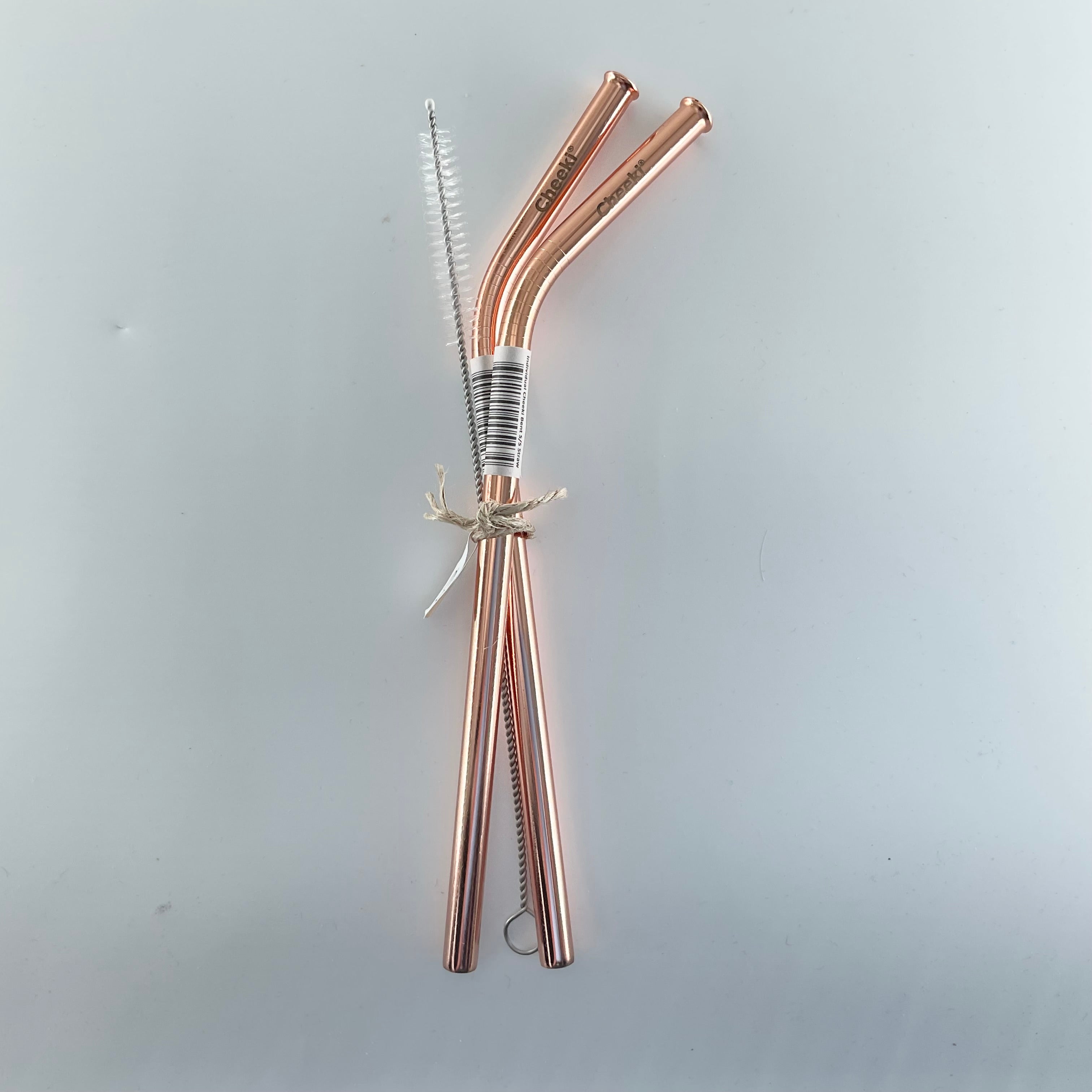 Set of rose gold metal straws with cleaning brush on a light gray background
