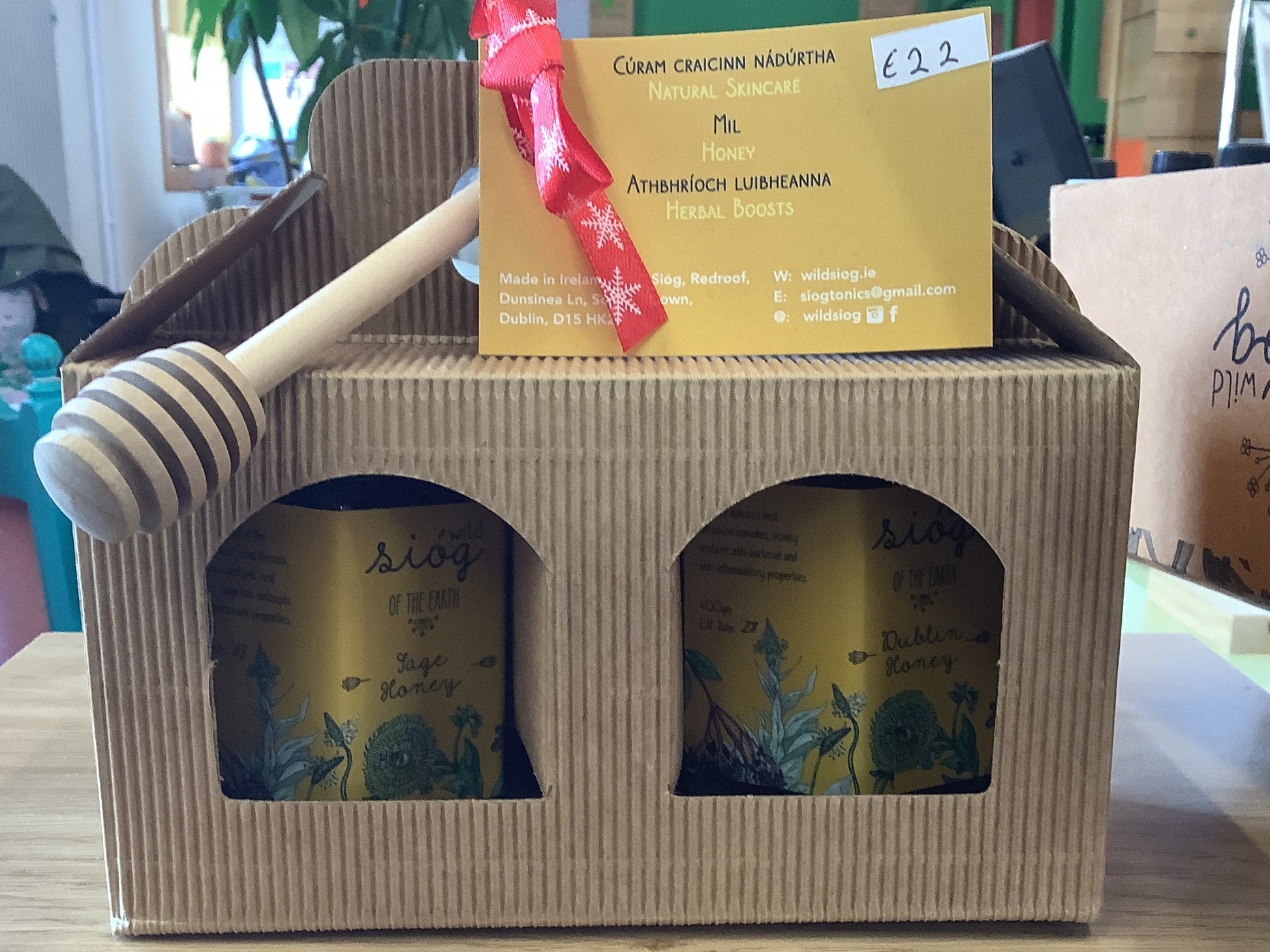 Two honey jars in a cardboard box with a honey dipper and a yellow label on a table.