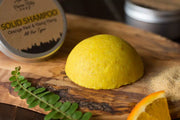 Yellow solid shampoo bar on a wooden board with a metal container labeled 'Solid Shampoo' in the background.