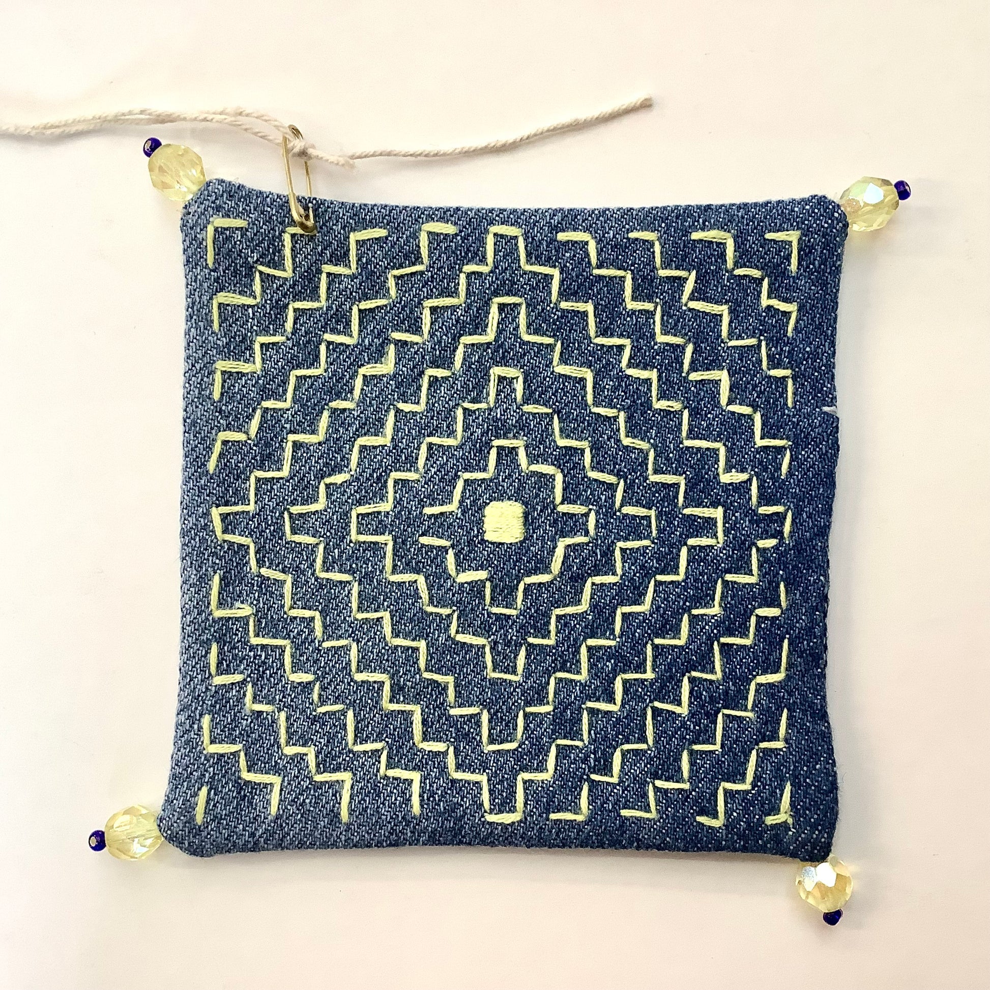Denim coaster with yellow geometric embroidery and yellow beads on each corner