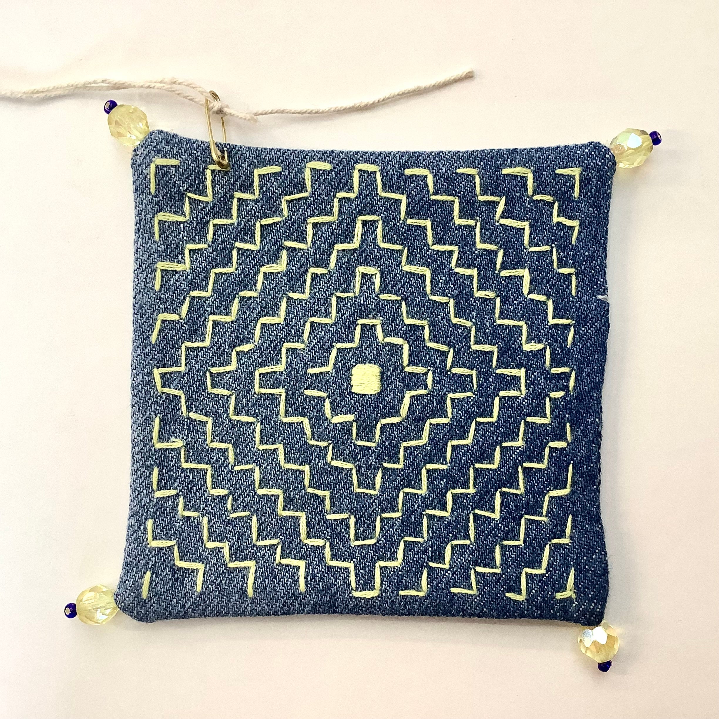Denim coaster with yellow geometric embroidery and yellow beads on each corner