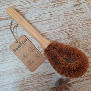 A beige dish brush with coconut bristles and a wooden handle, featuring a hanging tag with 'BAMBAW' branding.