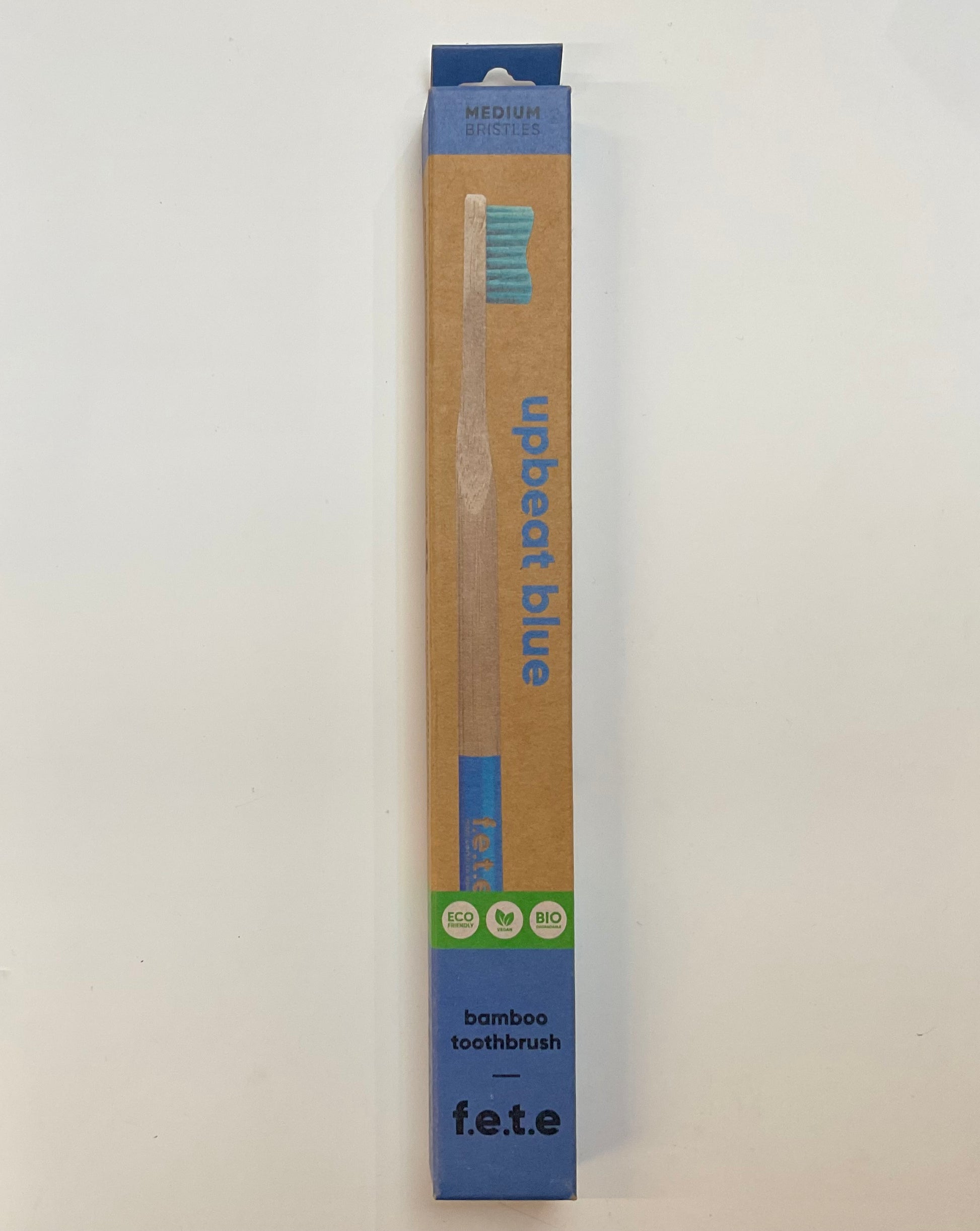A toothbrush in a cardboard packaging with a blue and green label, marked 'Upbeat Blue' and the brand 'F.E.T.E' visible.