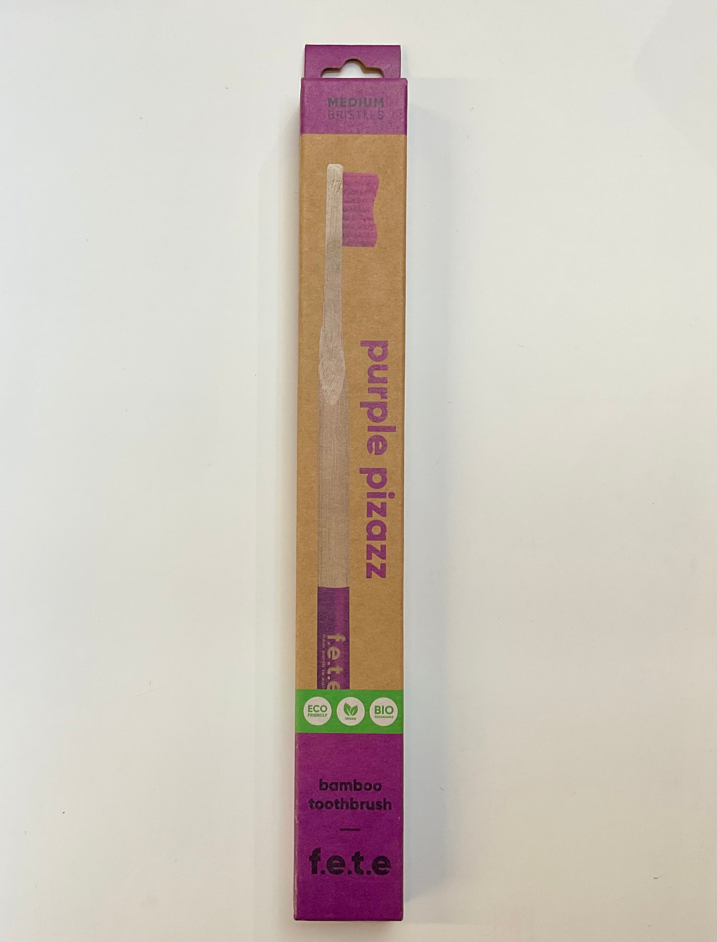 Packaging of 'Purple Pizazz Medium' toothbrush with eco-friendly packaging, including a bamboo handle and recycled materials.