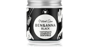A jar of Ben & Anna Black Natural Care Toothpaste on a white background with a subtle reflection. The jar has a black label with white illustrations and a silver metal cap.