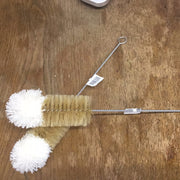 A bottle brush with natural fibers, featuring a wooden handle and white bristles with a product label attached.