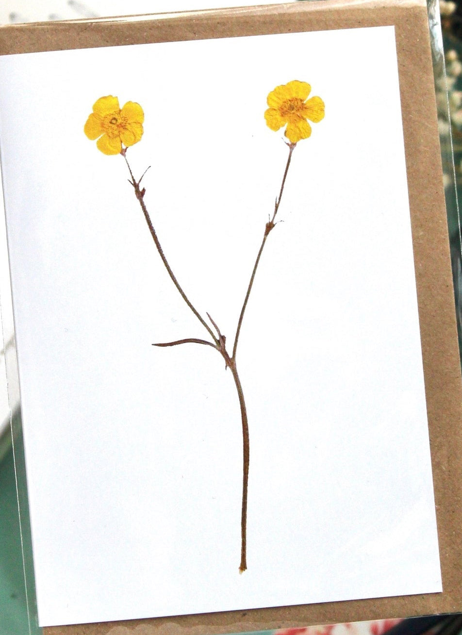 Greeting card with yellow flowers on a white background, placed on a green surface with stationery items.
