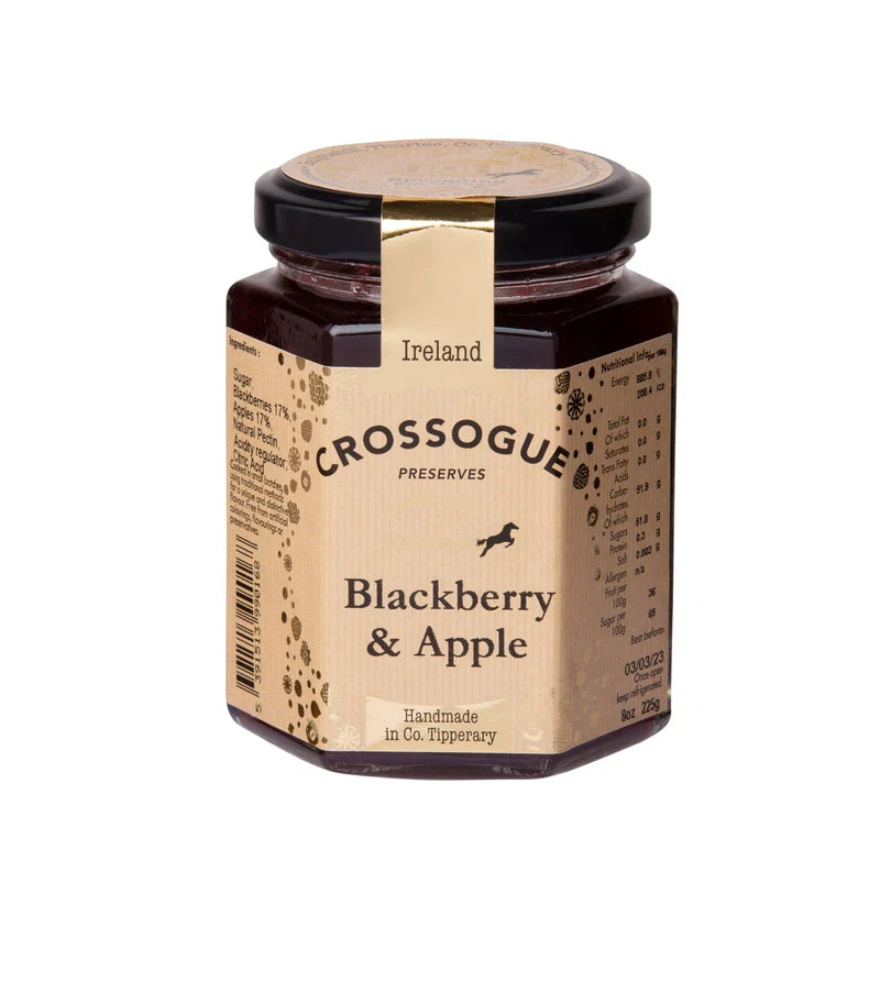 A jar of Crossogue Preserves Blackberry & Apple on a plain white background. The hexagonal glass jar contains a dark red jam, featuring a beige paper label with black text and a gold band around the neck, topped with a black lid.