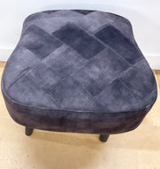 Gray quilted ottoman on a light wooden floor with a white wall background