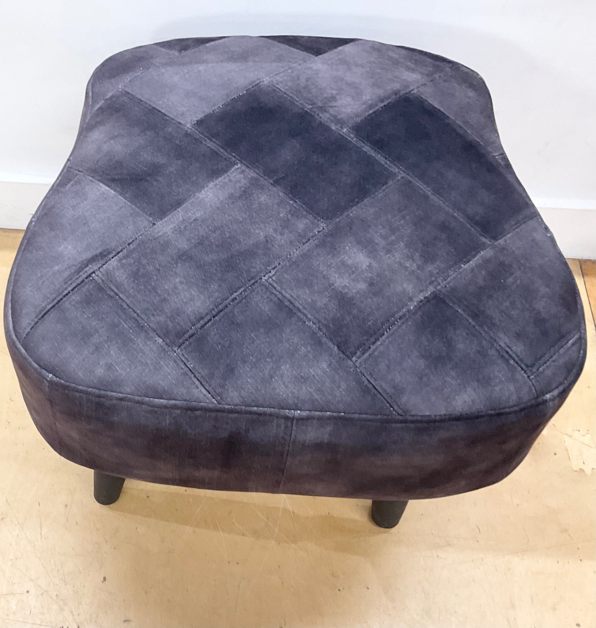 Gray quilted ottoman on a light wooden floor with a white wall background