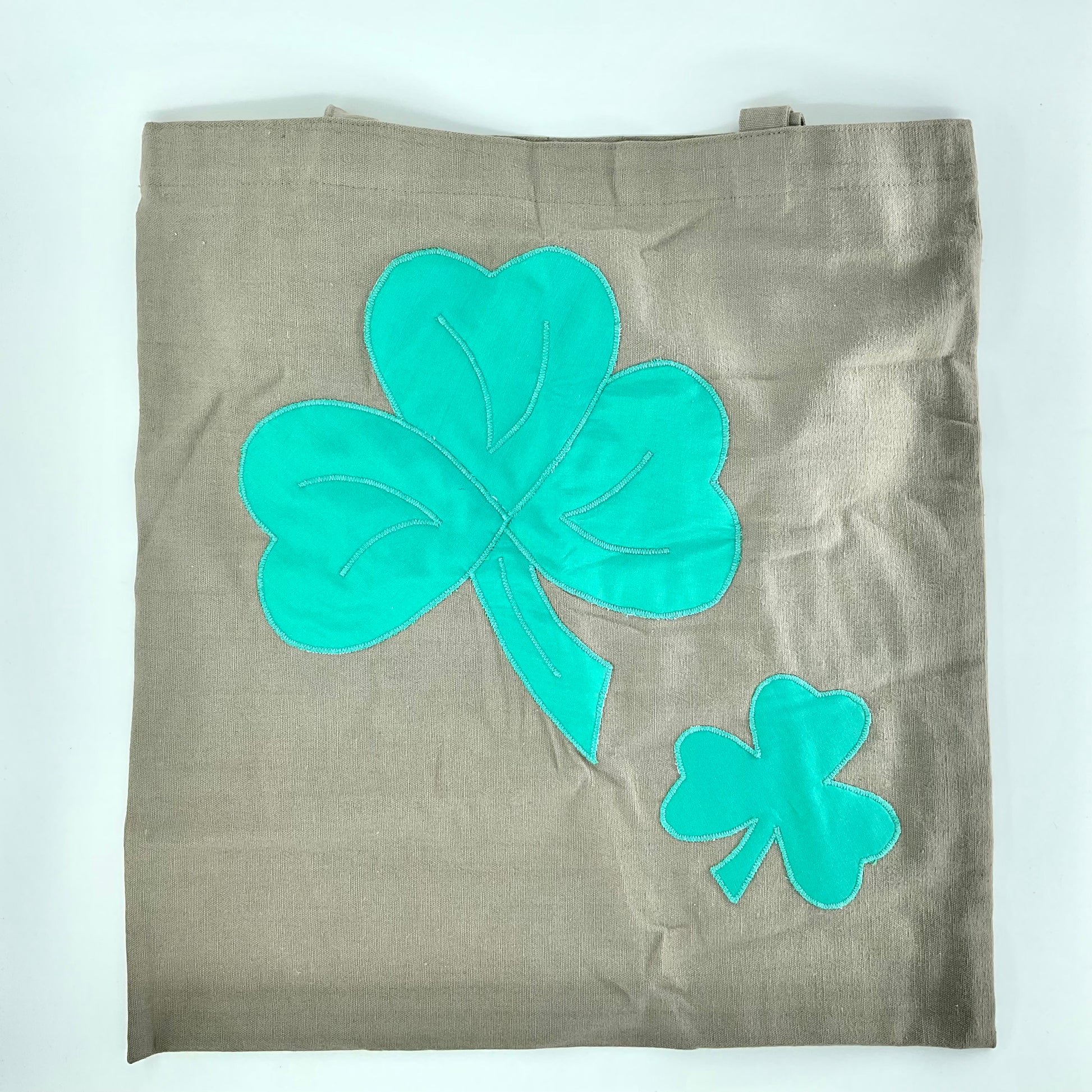 Brown tote bag with teal four-leaf clover designs on a white background