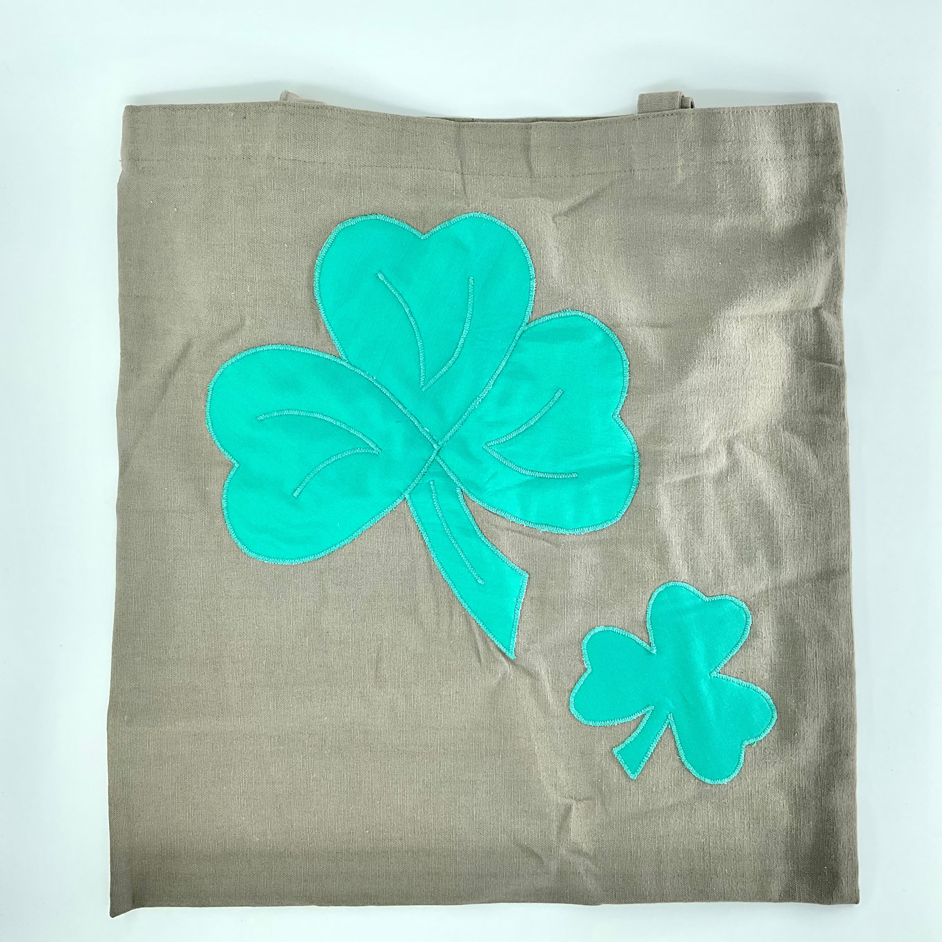 Brown tote bag with teal four-leaf clover designs on a white background