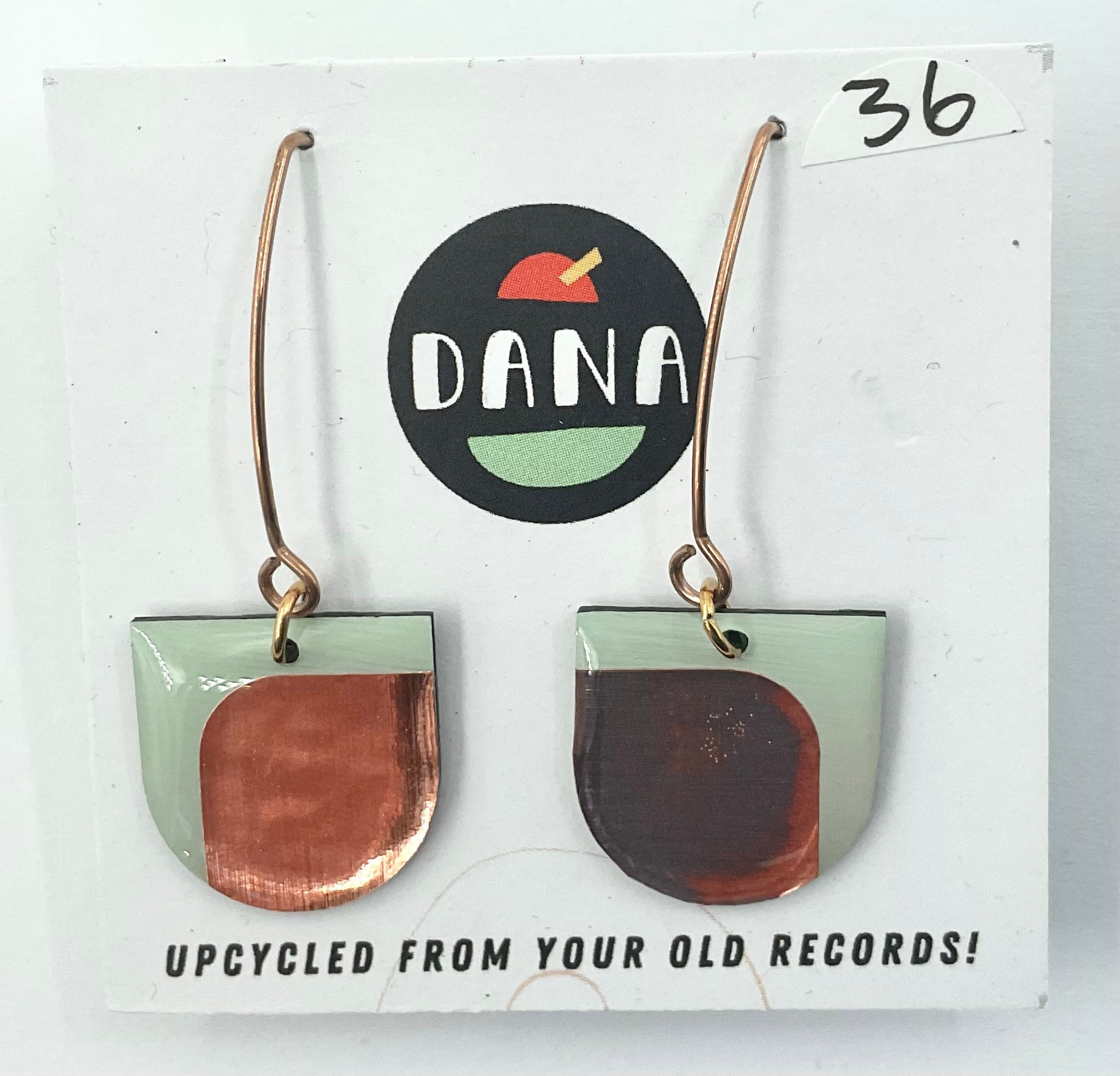 A pair of green and metallic details earrings, with the brand name Dana displayed on the packaging, indicating they are upcycled from old records.