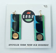 A pair of Dana Jewellery earrings made from upcycled vinyl records, featuring long rectangle shapes in green, mint, and gold colors, displayed on a white background with the brand logo and text.