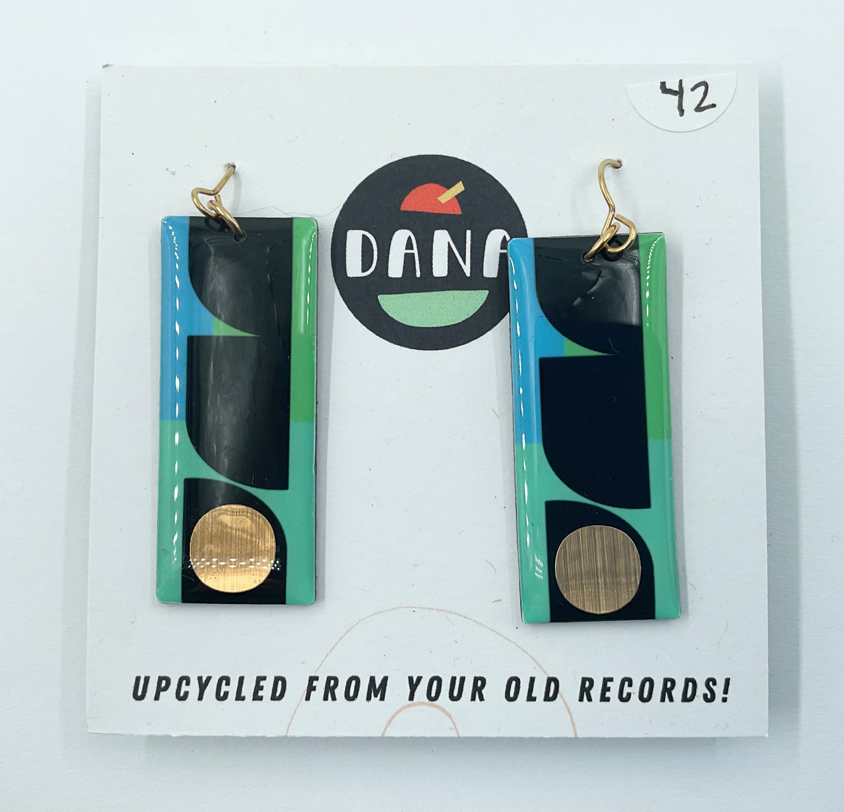 A pair of Dana Jewellery earrings made from upcycled vinyl records, featuring long rectangle shapes in green, mint, and gold colors, displayed on a white background with the brand logo and text.
