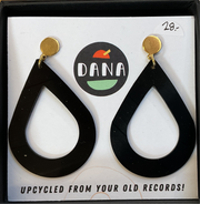 A pair of black teardrop-shaped earrings with gold-colored hoop earrings, displayed in a case with a 'Dana' brand mark and a tagline that reads 'UPCYCLED FROM YOUR OLD RECORDS!'.
