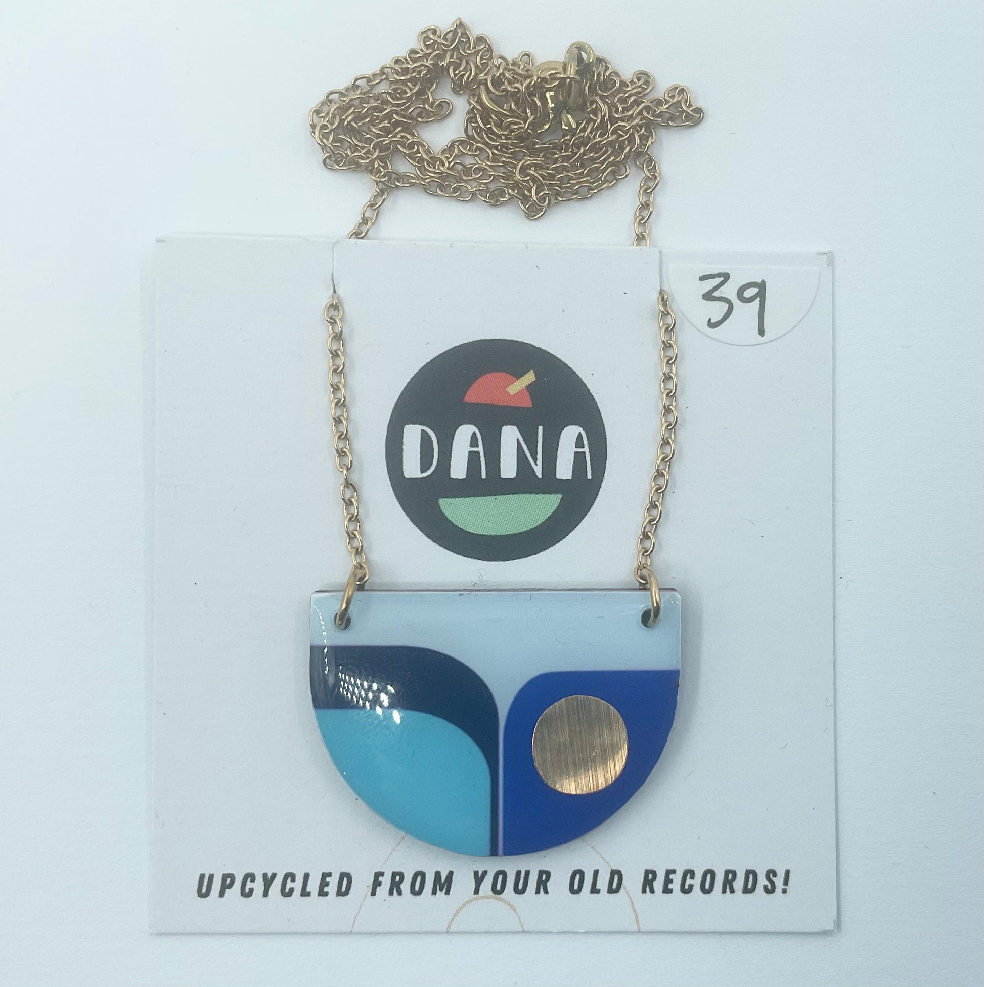 A blue and gold colored necklace with a unique geometric pendant, displayed on a card that reads 'dana' and 'upcycled from your old records!' with the number 39 written on it.