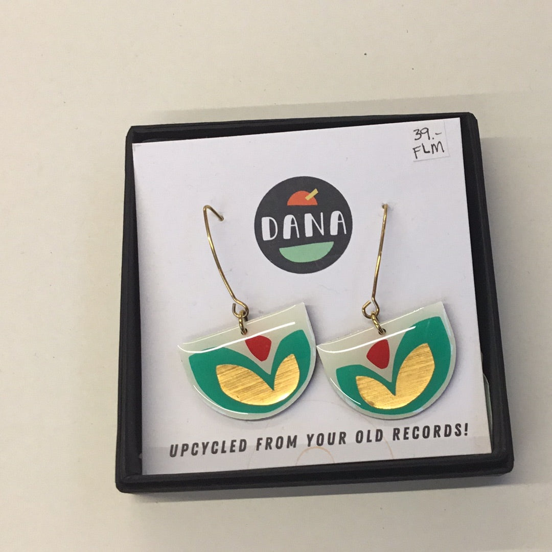 A pair of earrings designed with geometric shapes in white, turquoise, red, and bronze colors, presented on a black display card with the brand name 'DANA' at the top.