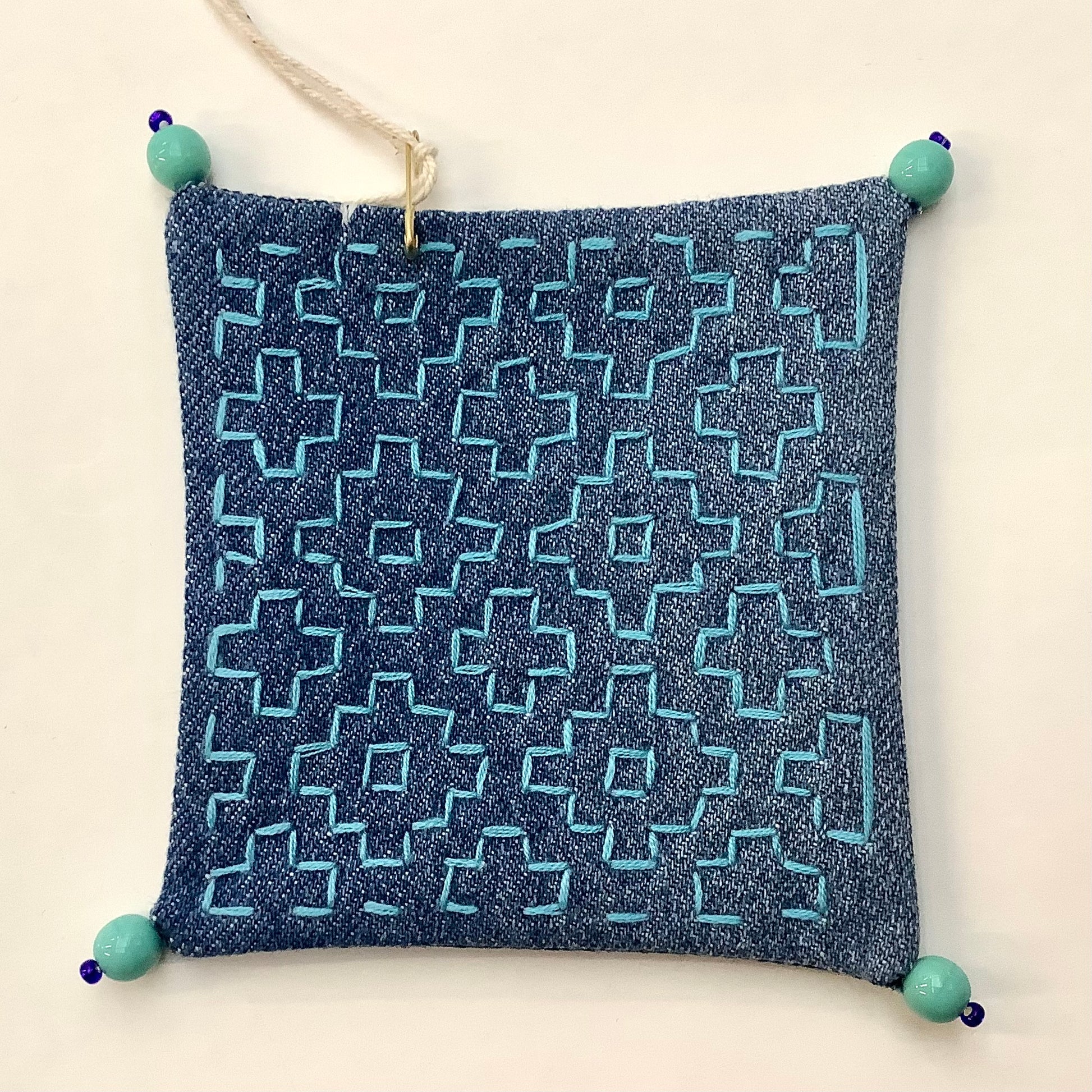 Coaster made from upcycled jeans with blue geometric embroidery and blue beads on each corner