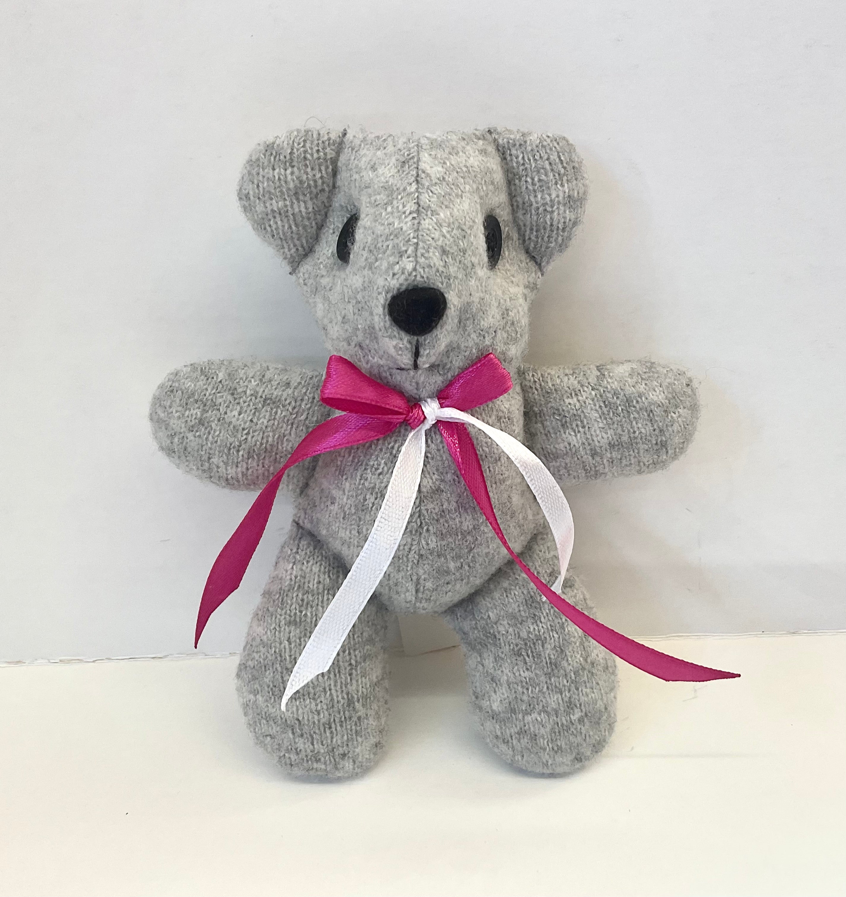 Gray teddy bear with a pink and white ribbon on a white background