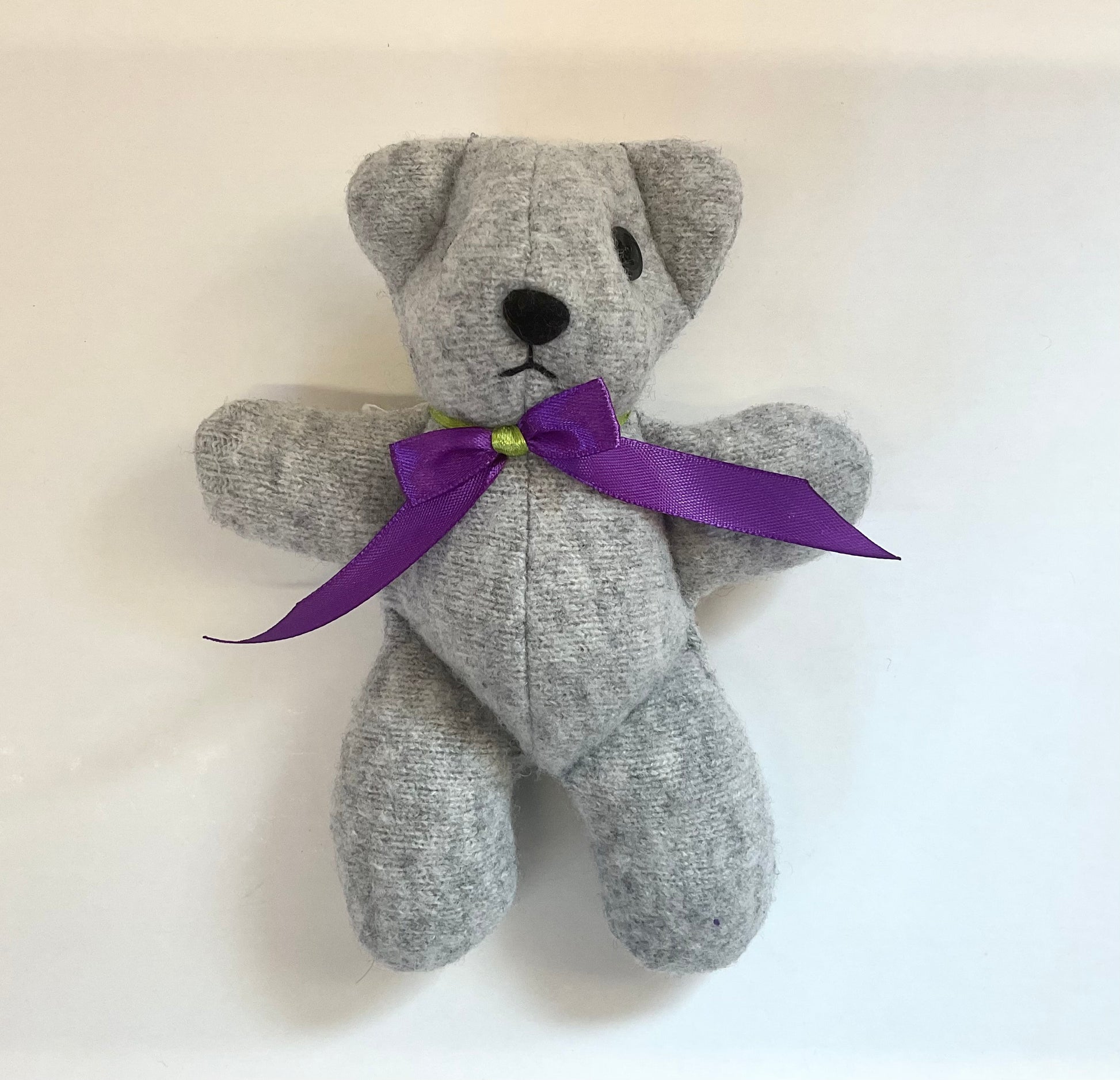 Grey teddy bear with a purple ribbon on a white background