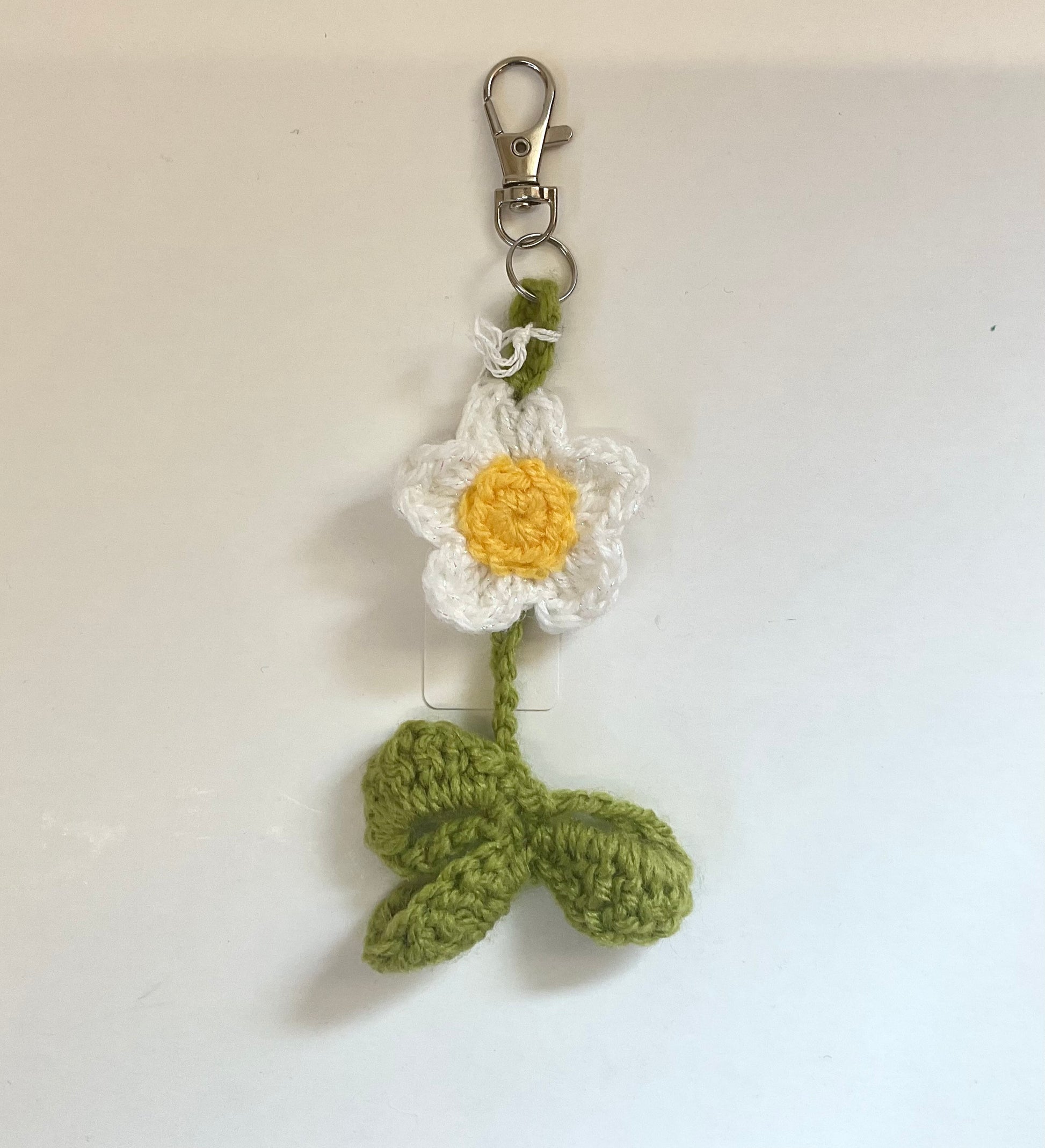 Crocheted white flower keychain with a yellow center and green stem on a white background