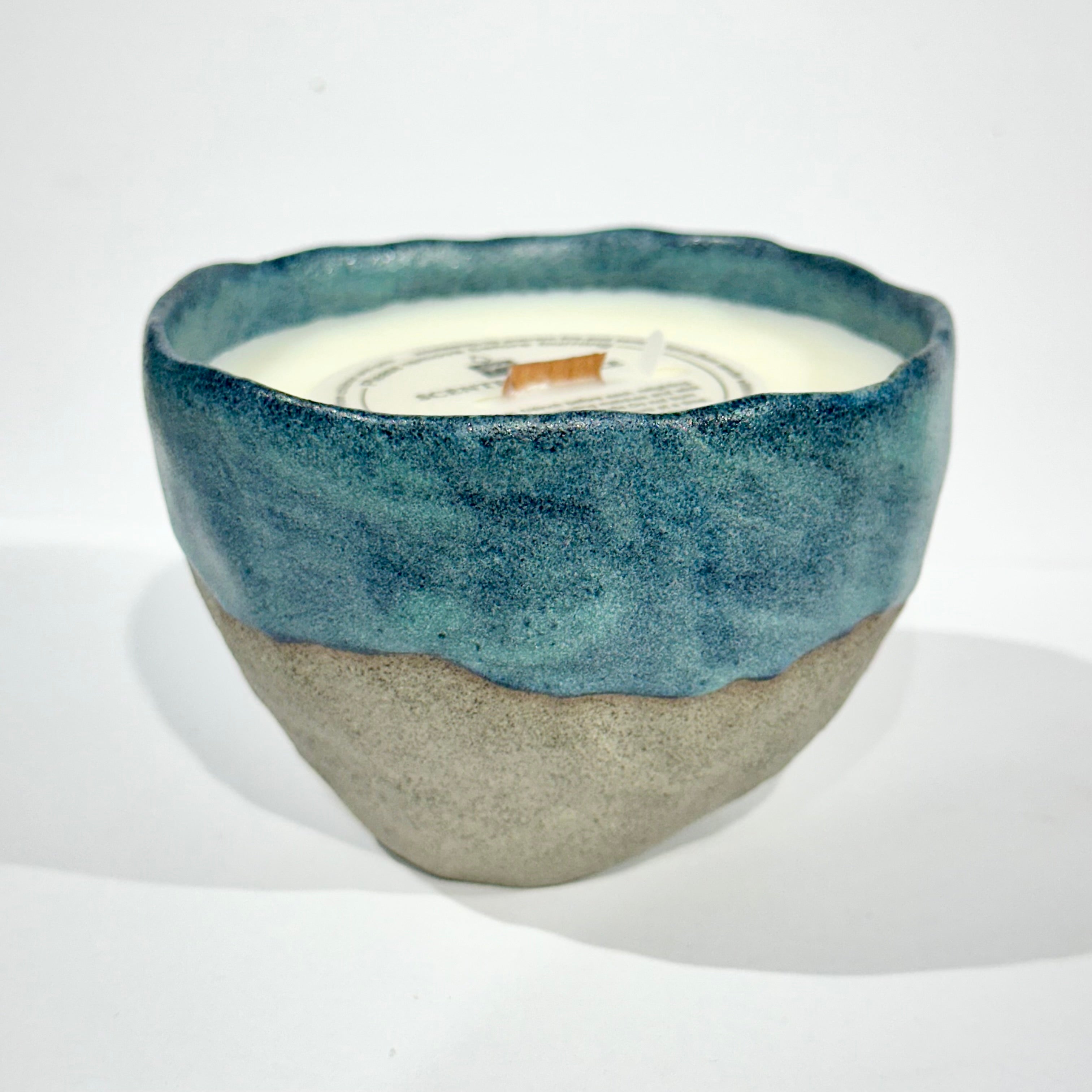 Handmade ceramic candle with blue and grey colors, placed on a white surface.
