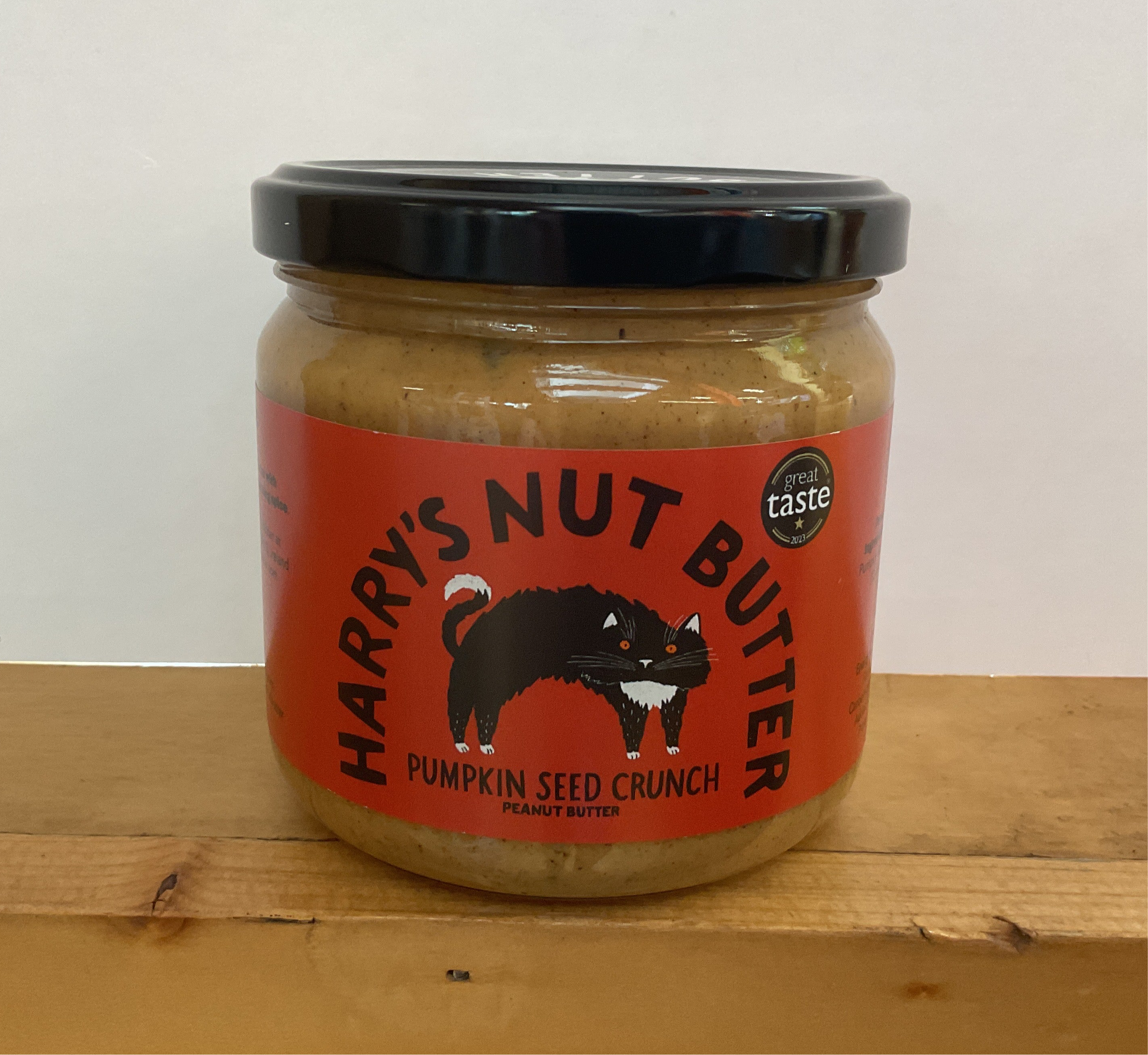 Jar of Harry's Nut Butter with a red label featuring a cat illustration on a wooden surface.