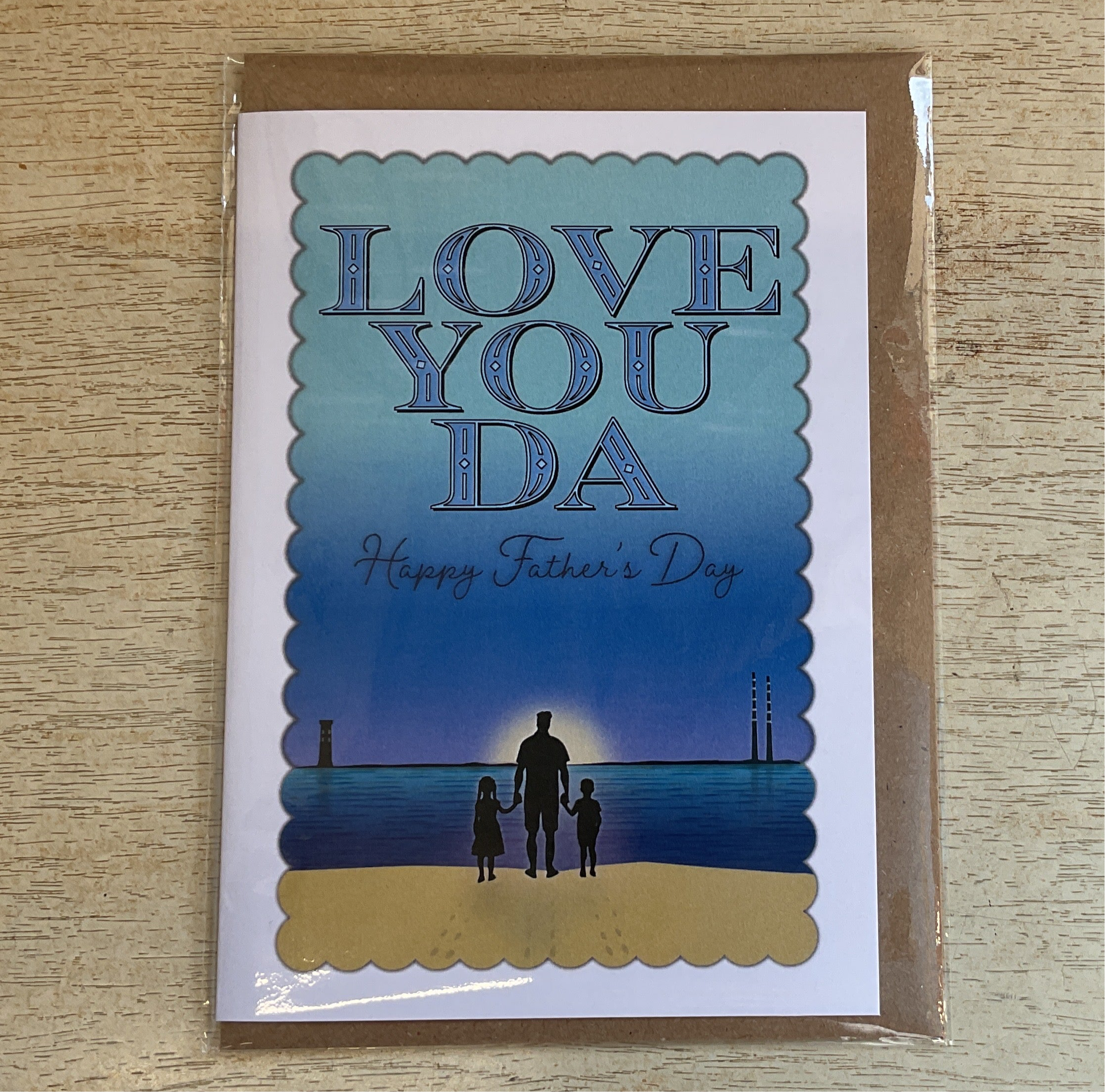 Greeting card with 'LOVE YOU DA Happy Father's Day' text and an illustration of a adult and two children on a beach at sunset