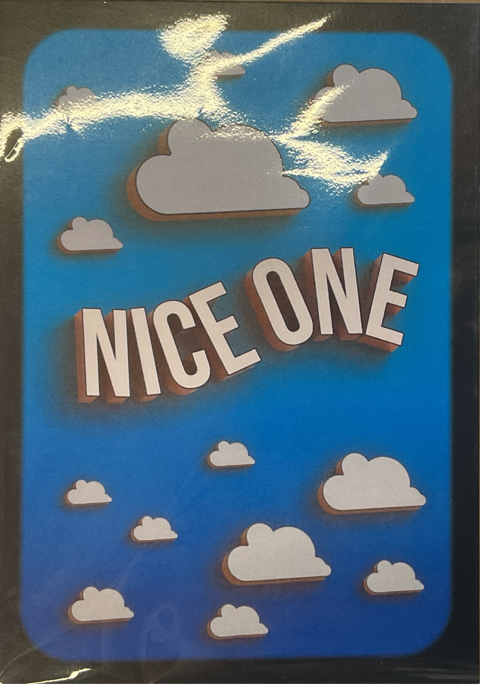 A greeting card with the phrase 'NICE ONE' printed in bold, capital letters, set against a blue background with cloud illustrations.