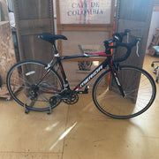 A black and red Merida road bicycle with white branding, displayed indoors on a stand against cardboard crates.