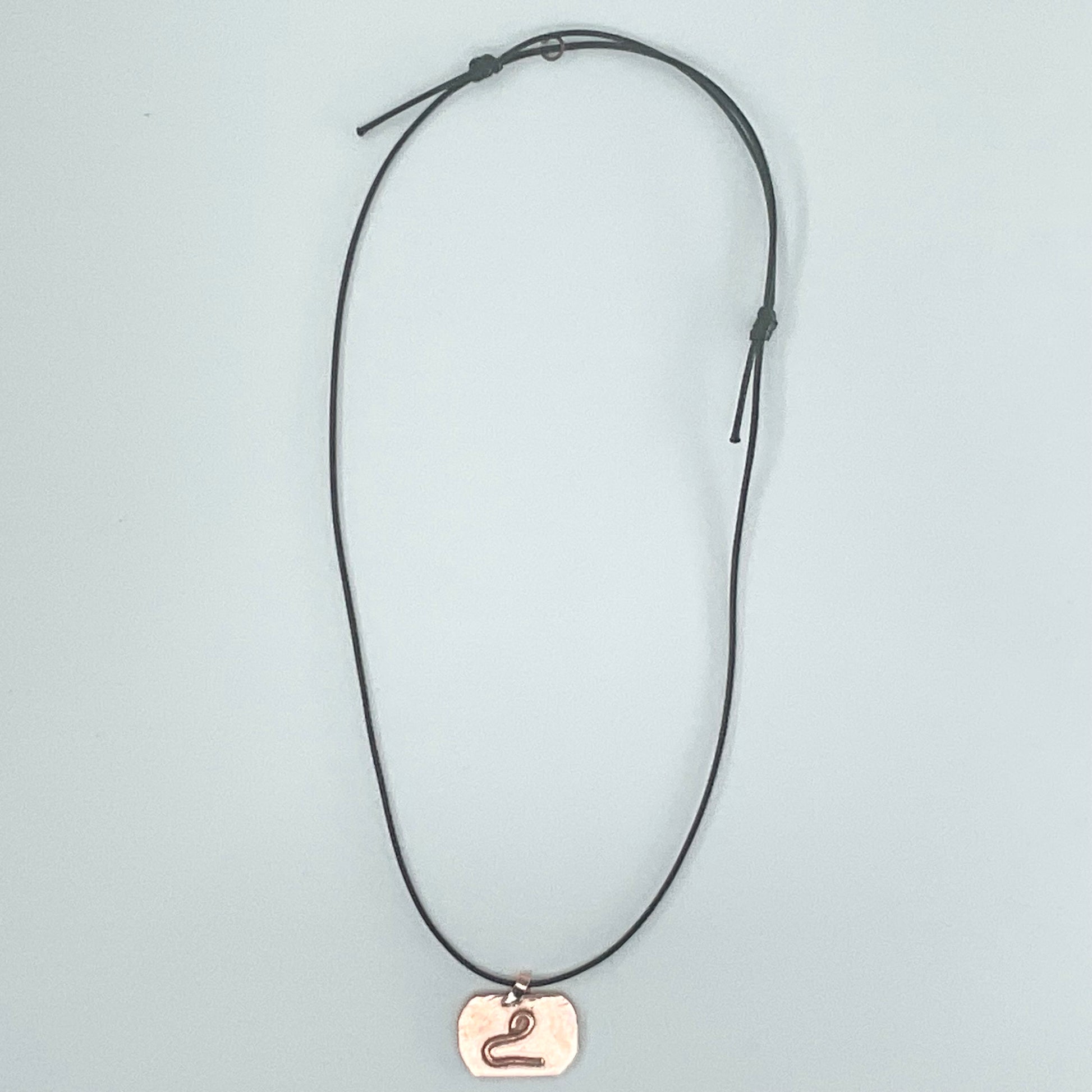 A black adjustable cord necklace featuring a small, polished rose gold pendant engraved with the Roman numeral 'II', displayed against a light gray background.