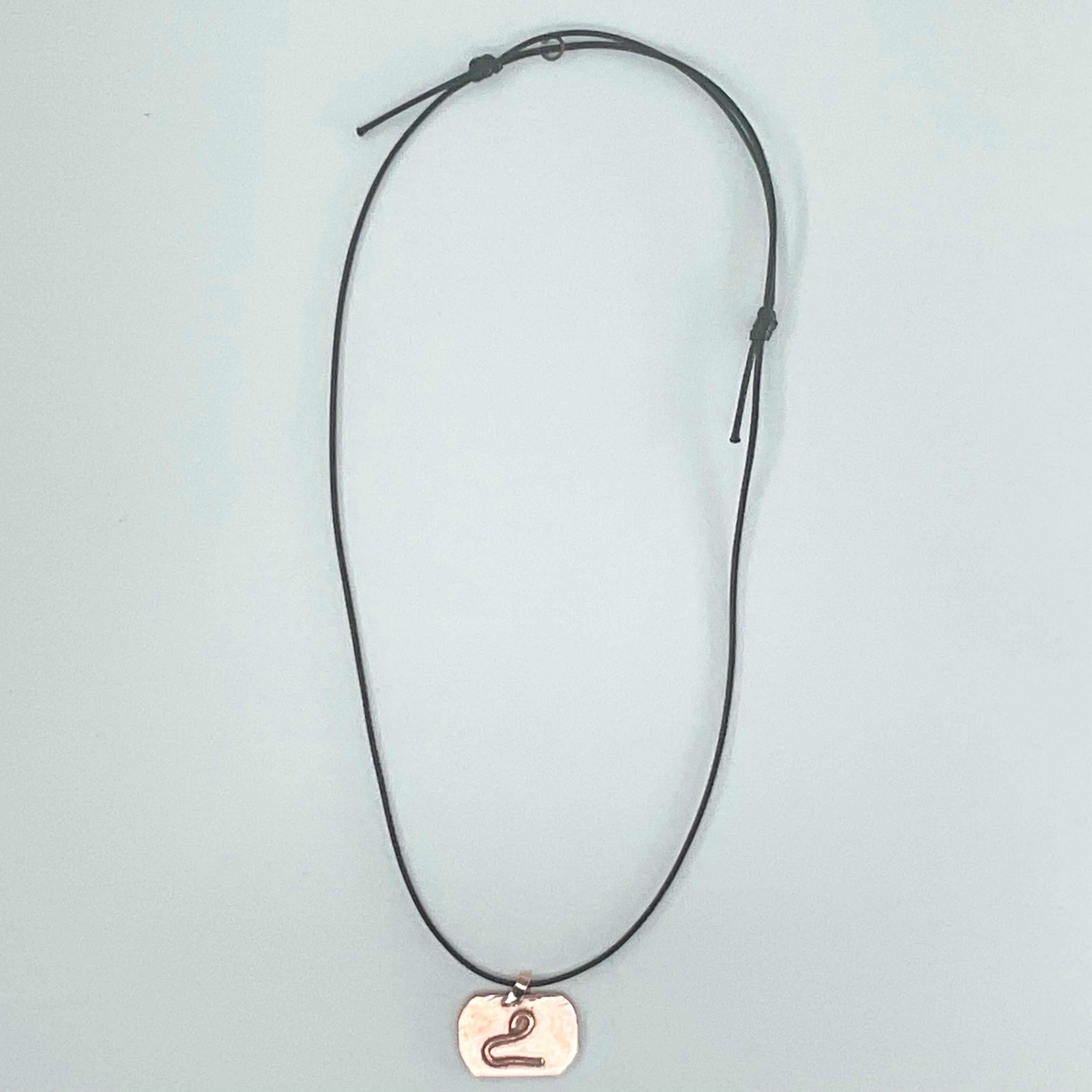 A black adjustable cord necklace featuring a small, polished rose gold pendant engraved with the Roman numeral 'II', displayed against a light gray background.