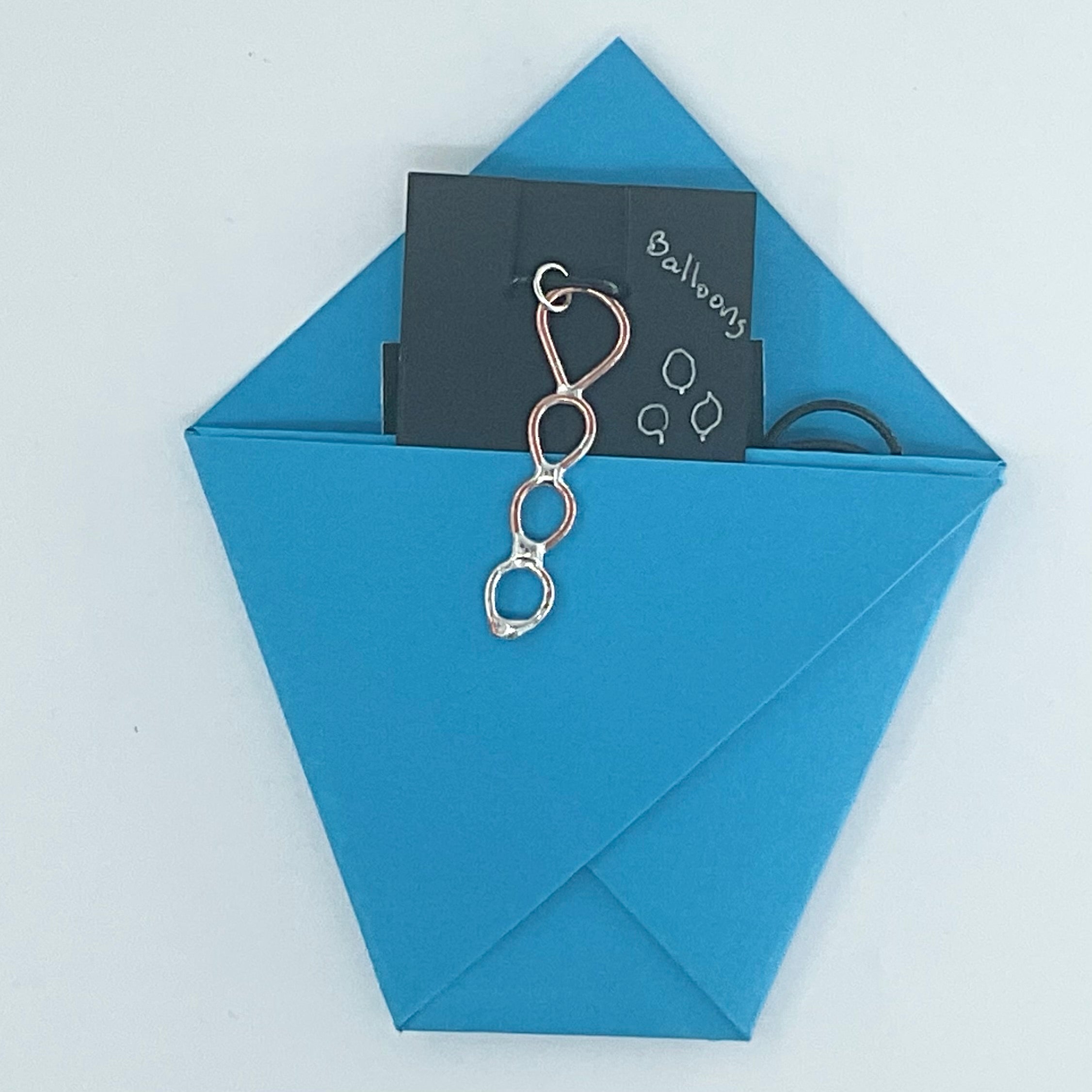 A blue paper envelope or pouch on a white background, with a black card partially pulled out and a silver metal clasp hanging from it. The card has the word 'Balloon' written on it.