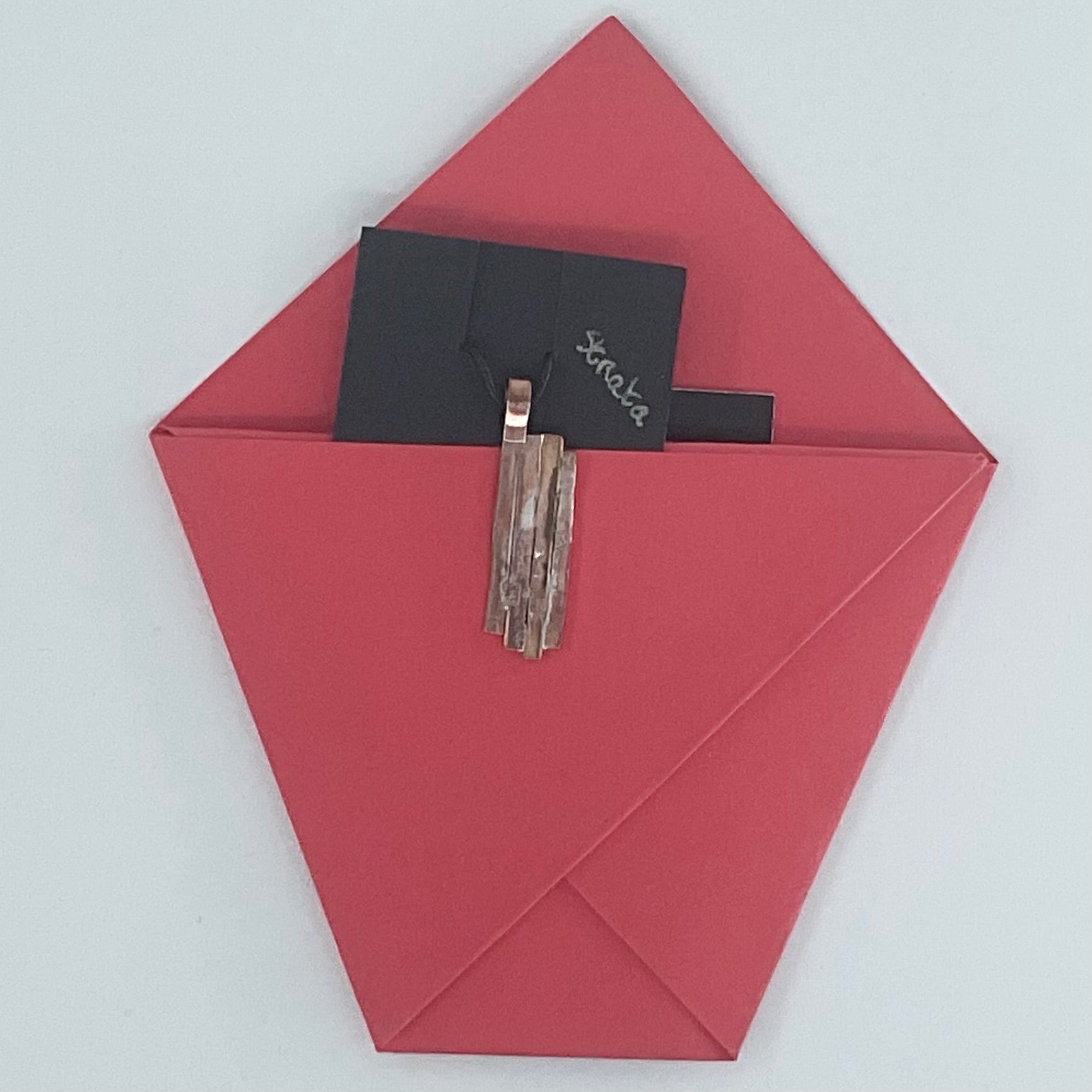 A red paper envelope or pocket holding a black card with the word 'serala' and a metallic tassel accessory, photographed against a plain light background.