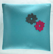 Teal pillow with two felt flowers, one gray and one pink, on a white background