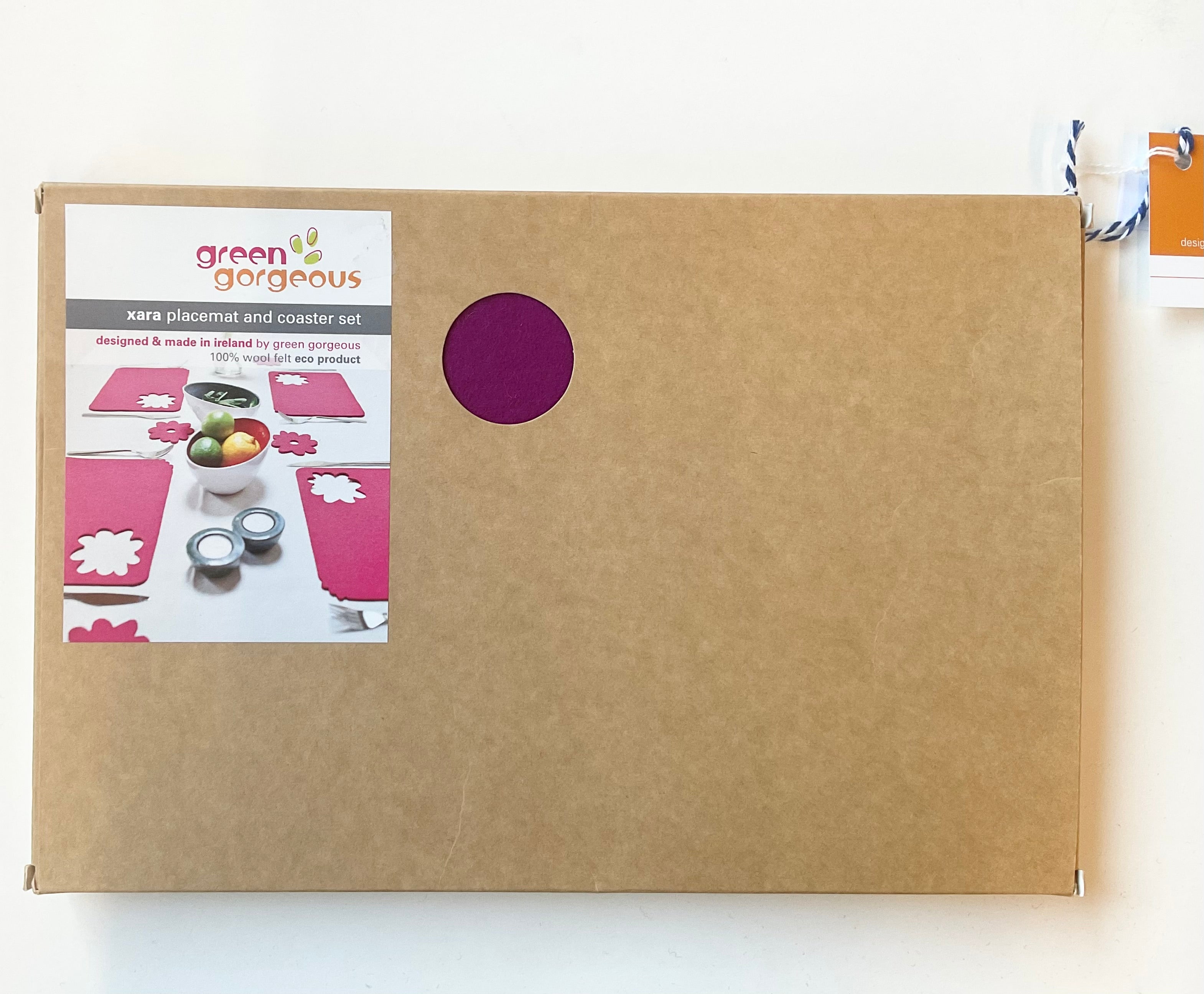 Brown box with a window displaying pink placemats and coasters, branded 'Green Gorgeous'.