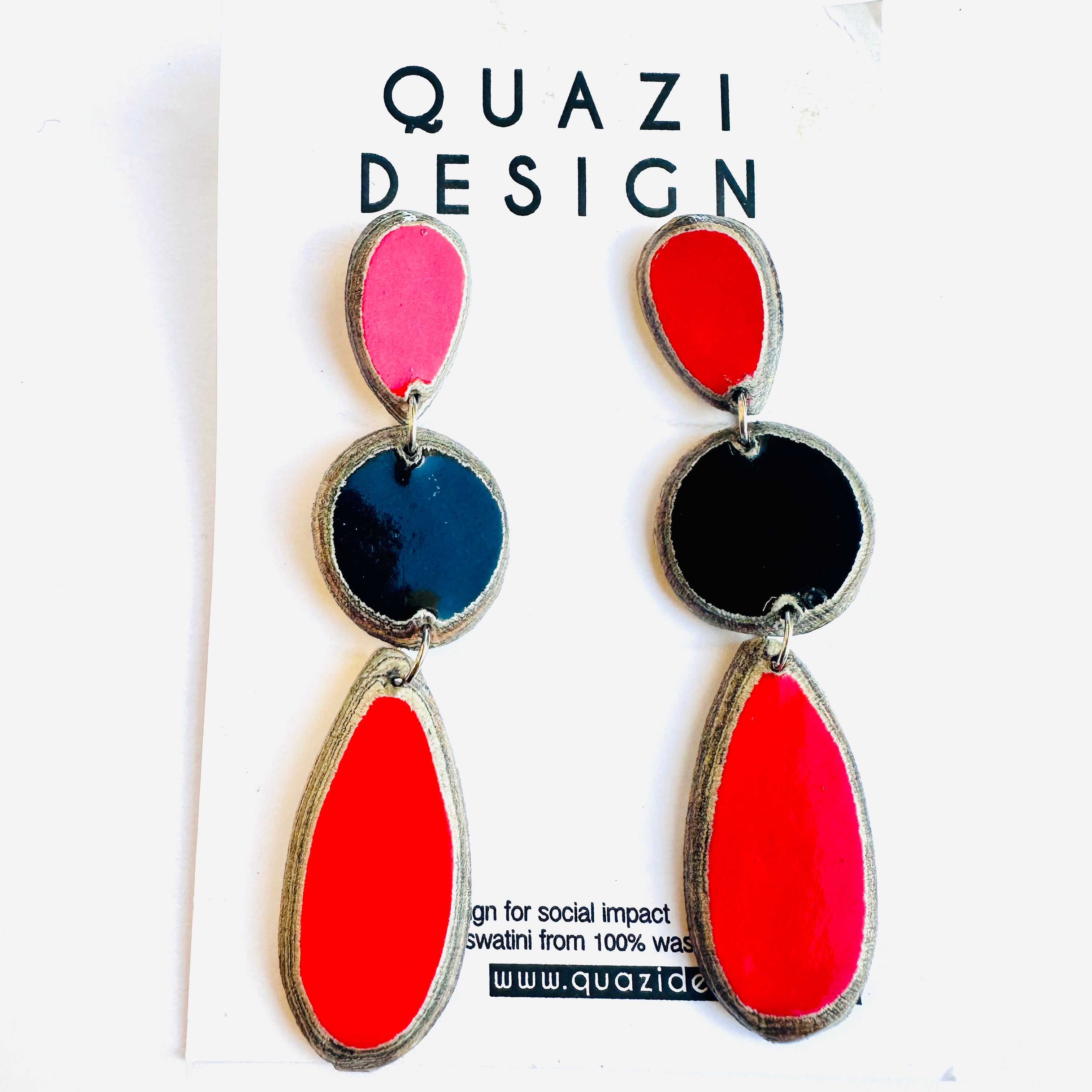 A pair of earrings with red, black, and pink geometric shapes, displayed on a white card with 'Quazi Design' text.