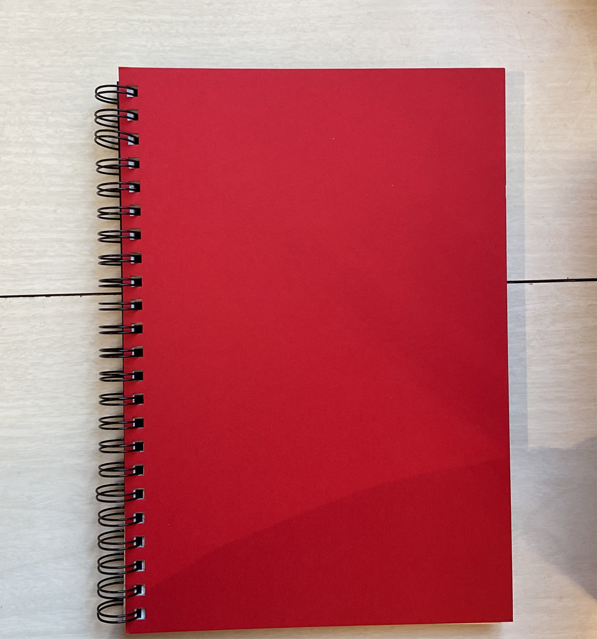 A red hardcover notebook with a wire binding, A4 size, lying flat on a surface.