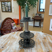 A black bicycle disc and chainring candle holder with a green candle on top, displayed on a rustic wooden table in a vintage-style room.