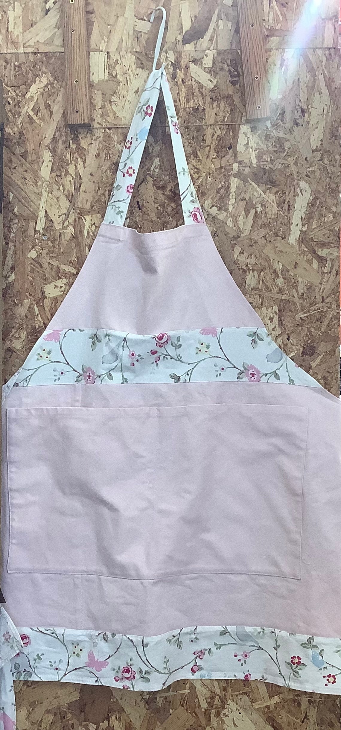Light purple apron with floral trim hanging on a wooden surface