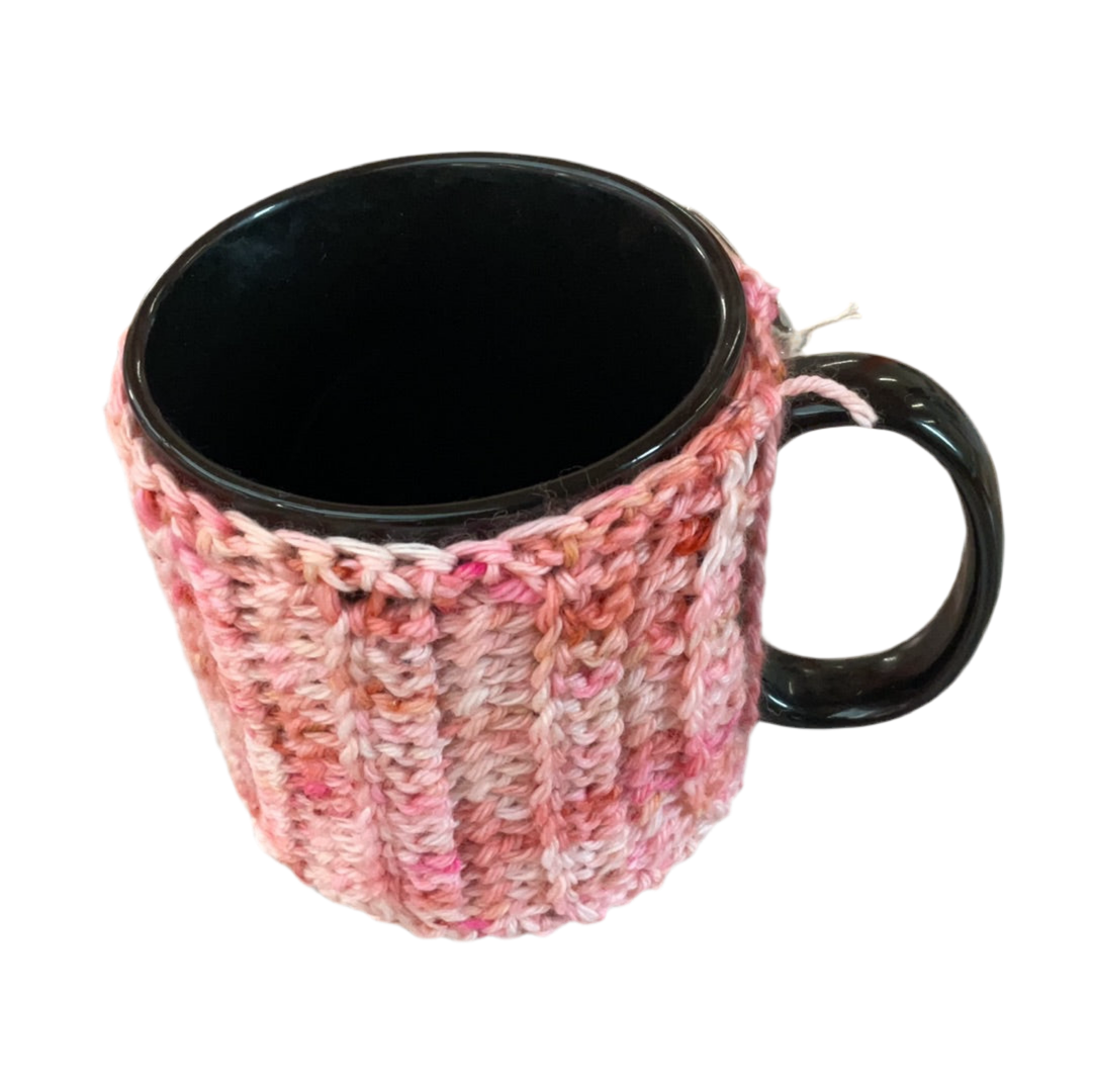 Black mug with a pink and white knitted cozy on a white background