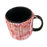 Black mug with a pink and white knitted cozy on a white background