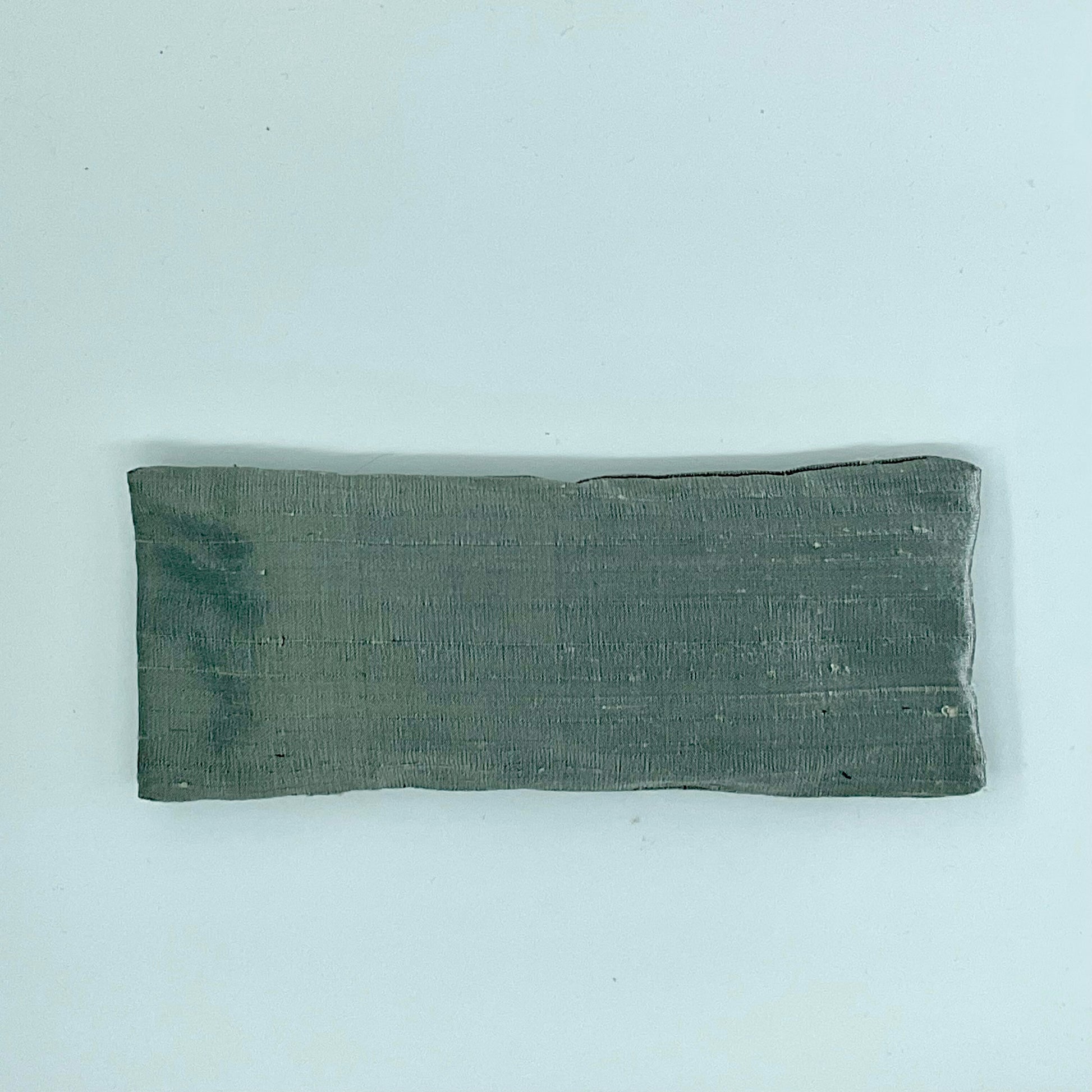 A gray silk eye mask laid flat on a white background.