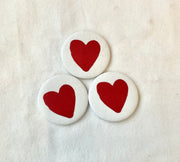 Three round white badges with red heart designs on a light beige background