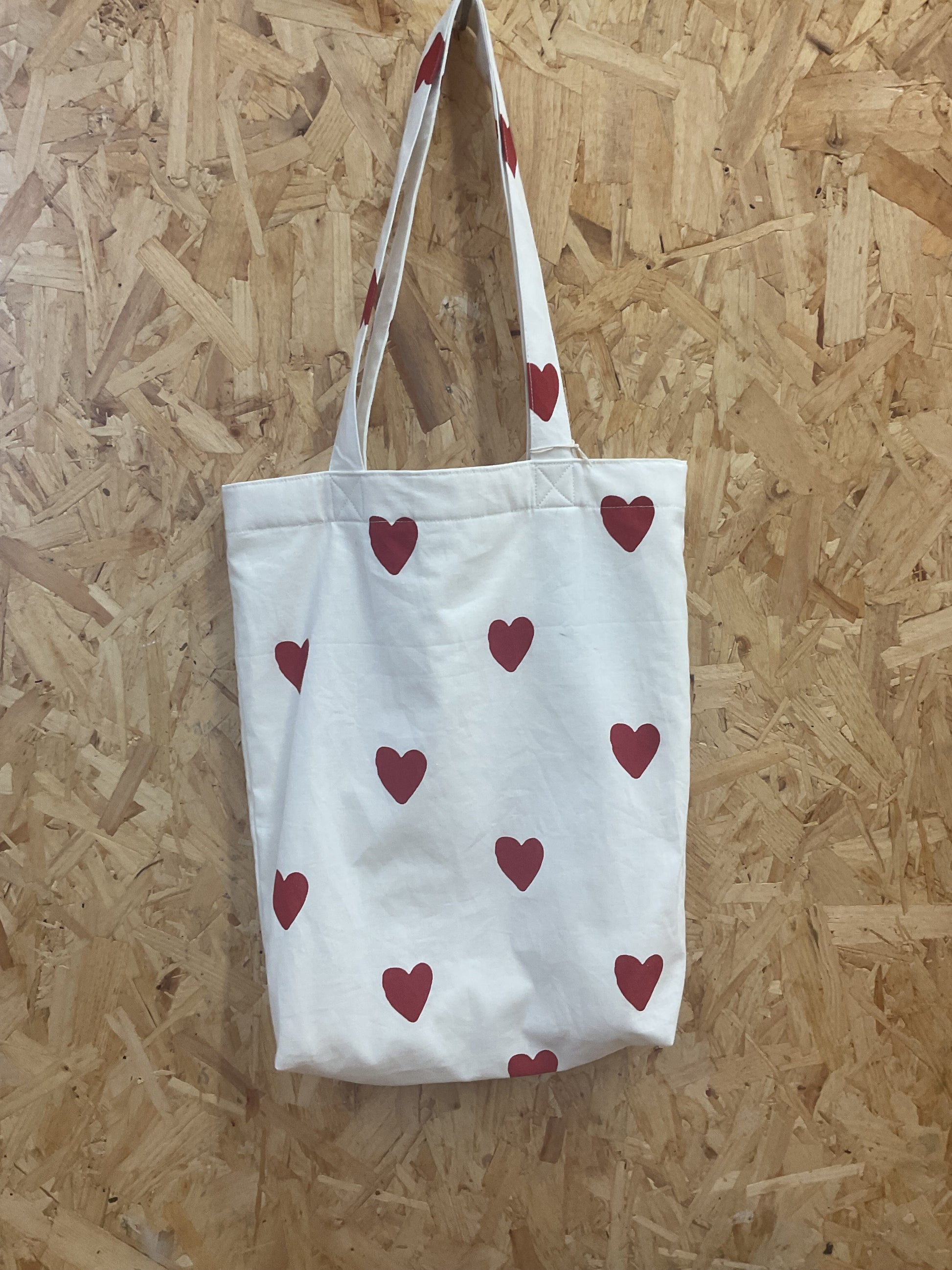 White tote bag with red heart patterns on a wooden floor